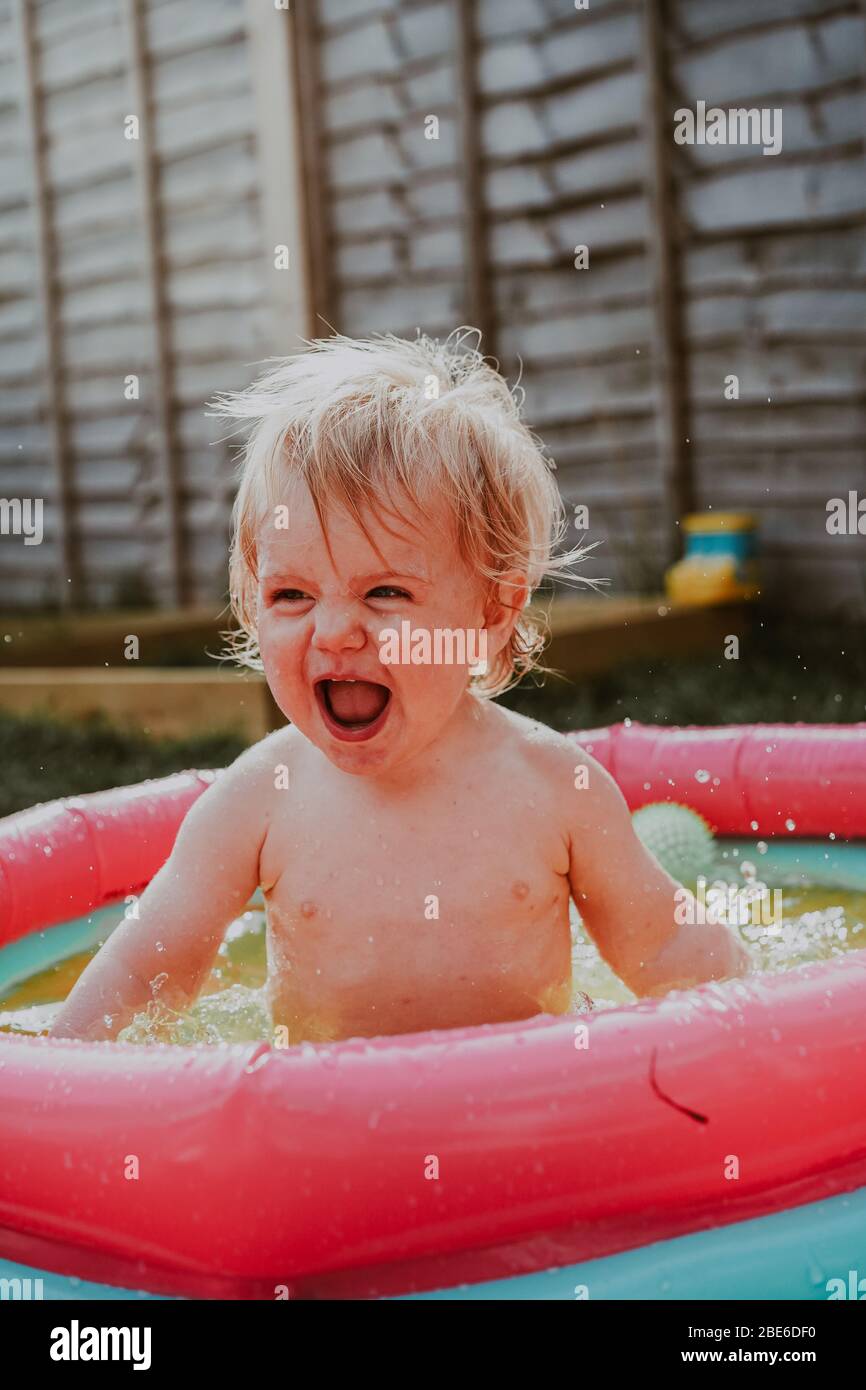 Pequeño robot niño jugando en la piscina infantil en el jardín en verano, Reino Unido Foto de stock