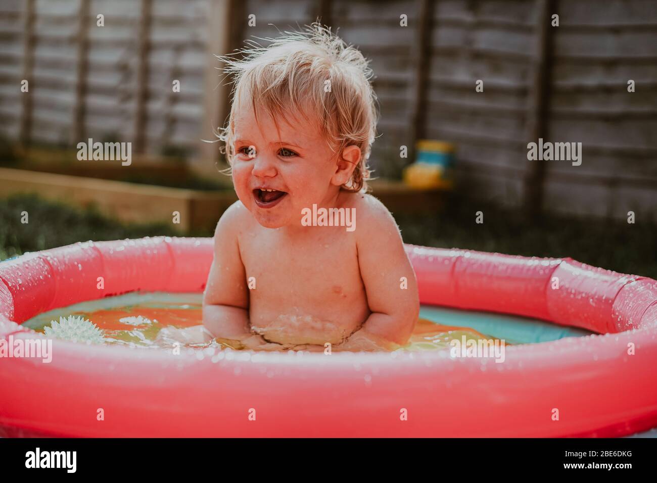 Pequeño robot niño jugando en la piscina infantil en el jardín en verano, Reino Unido Foto de stock