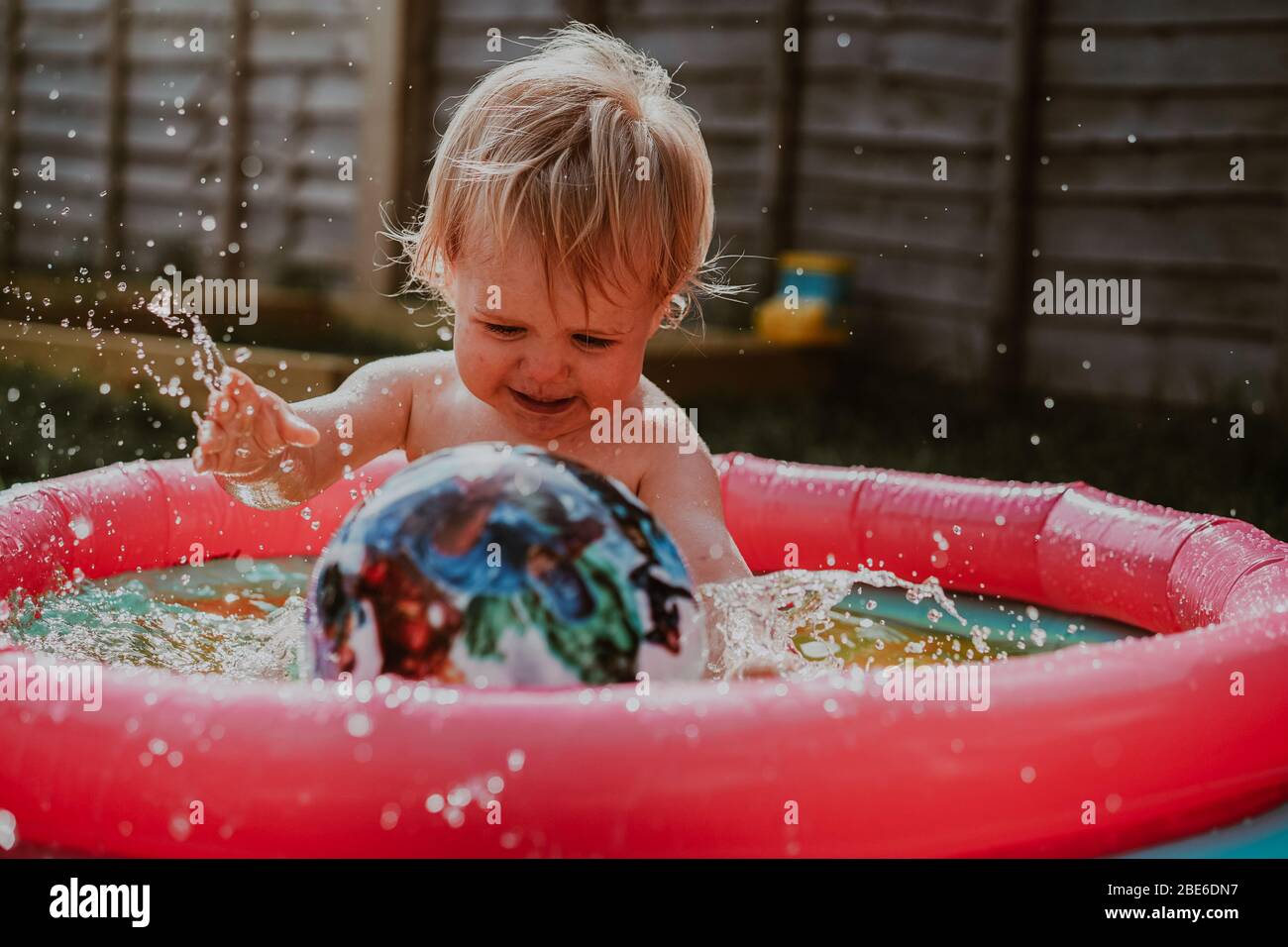 Pequeño robot niño jugando en la piscina infantil en el jardín en verano, Reino Unido Foto de stock