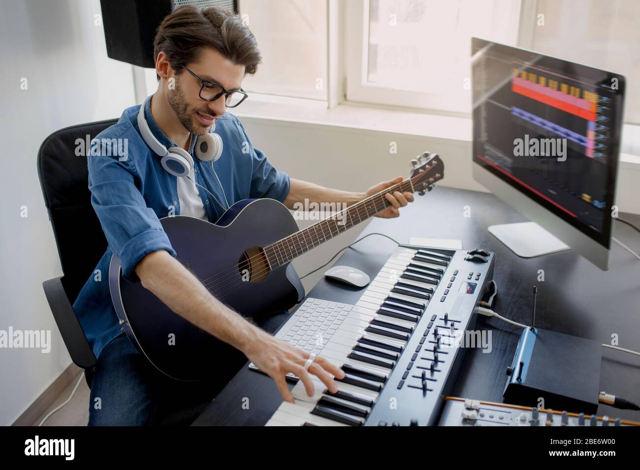 Man toca la guitarra y produce banda sonora electrónica o pista en el  proyecto en casa. Arreglista de música masculina que compone la canción en  el piano midi y el equipo de
