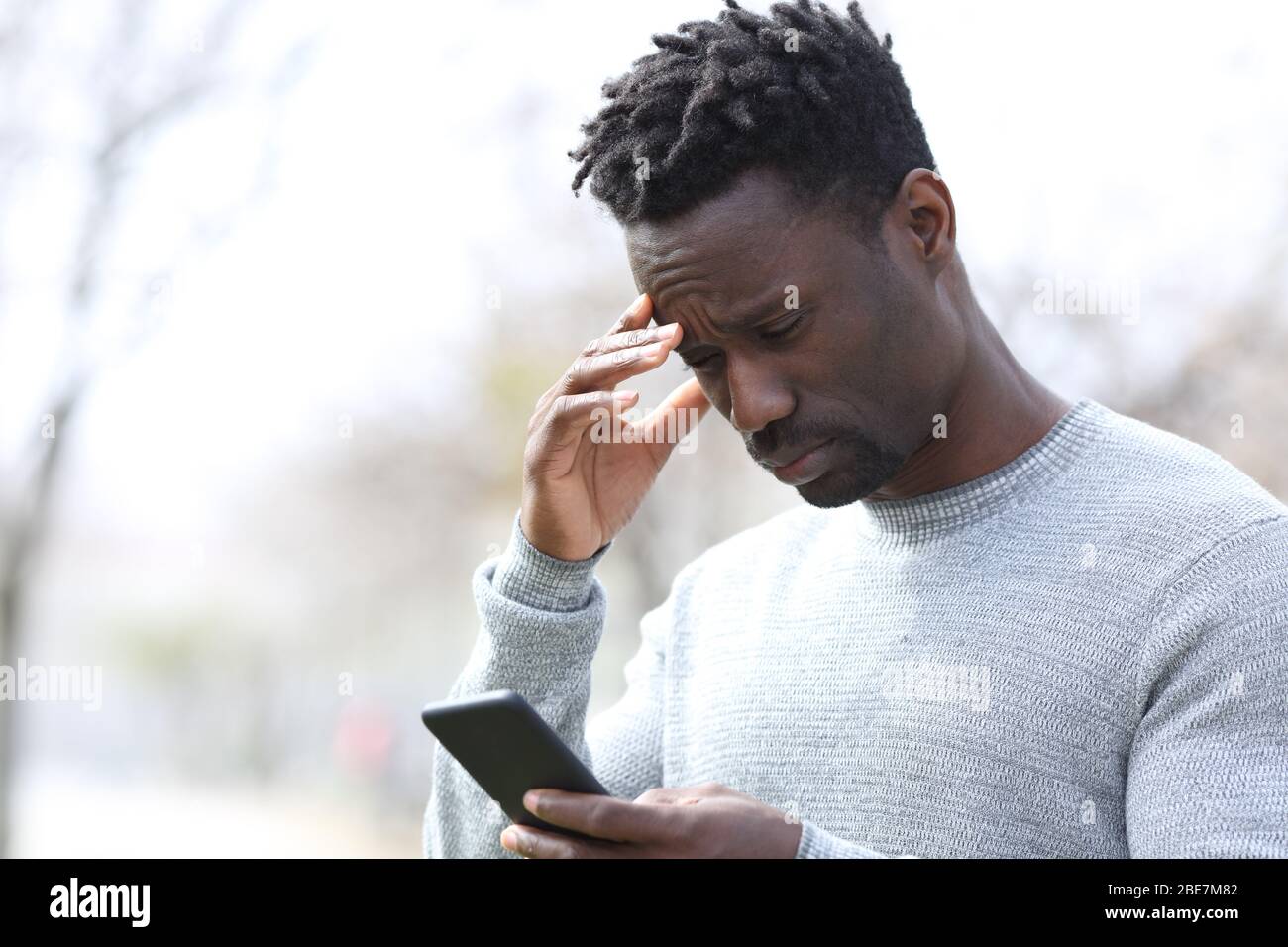 Hombre negro preocupado leyendo malas noticias en el teléfono inteligente de pie en el parque Foto de stock