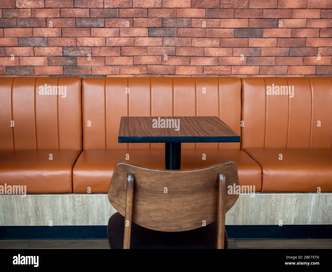 Decoración de muebles en estilo café retro. Mesa de bar vacía de madera y sofá  de cuero largo naranja y silla de madera sobre fondo de pared de ladrillo  Fotografía de stock -