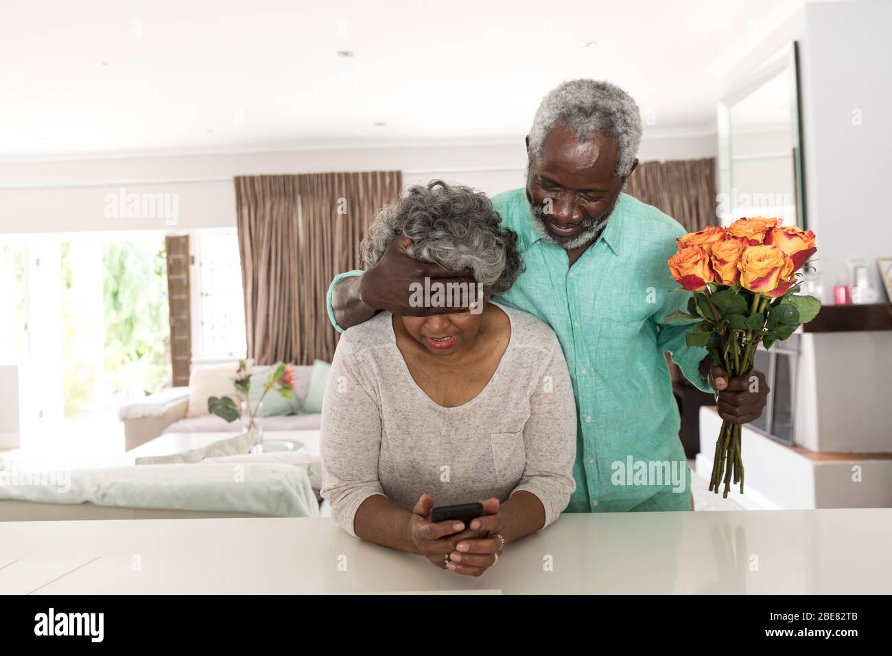 Un hombre afroamericano de mayor edad sorprendiendo a su esposa con flores Foto de stock