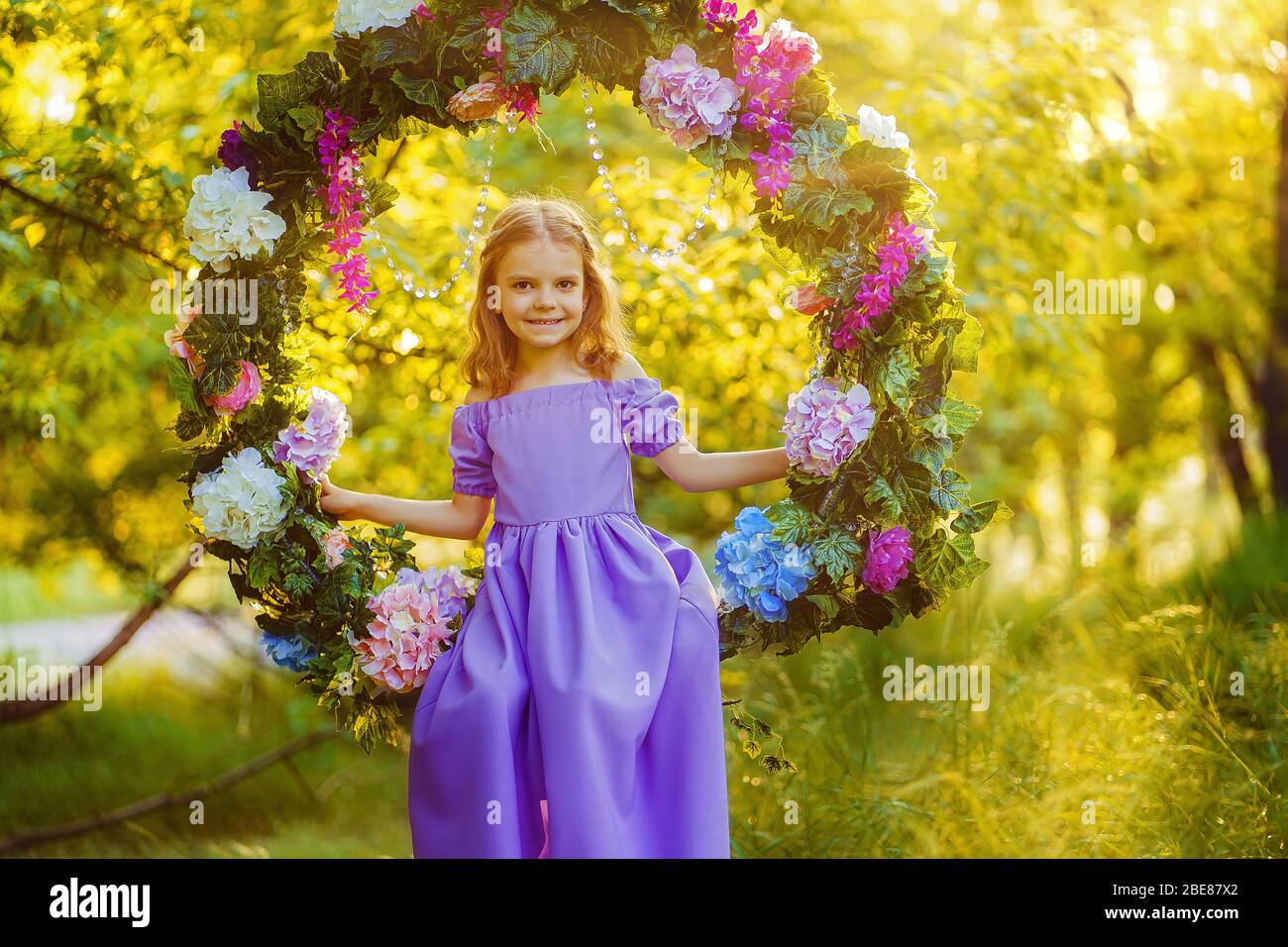 Linda niña con vestido lila posando mientras se sienta en anillo decorado  con flores en el parque de verano Fotografía de stock - Alamy