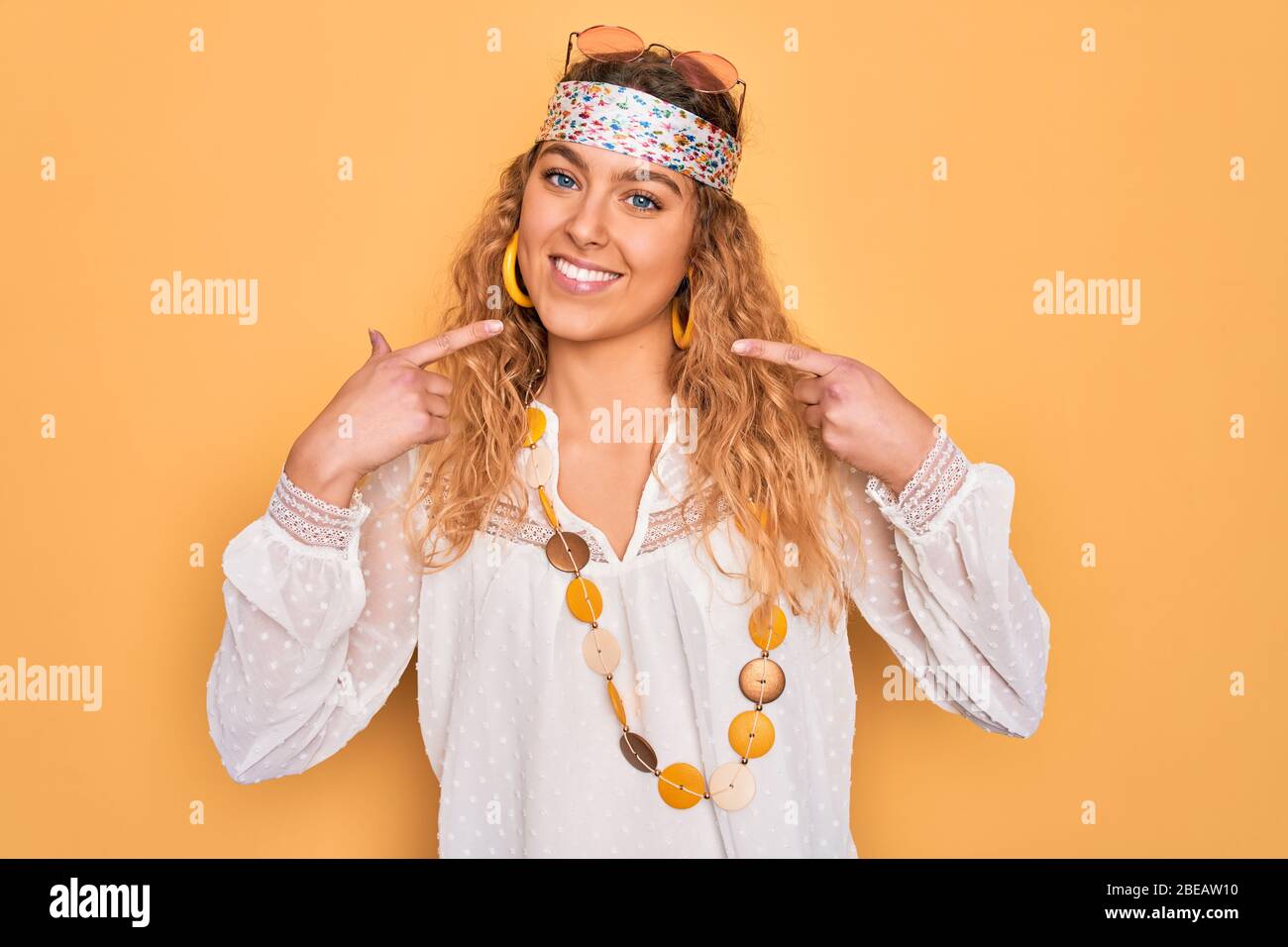 Joven hermosa mujer rubia hippie con ojos azules con gafas de sol y  accesorios sonriendo alegre mostrando y señalando con los dedos dientes y  mou Fotografía de stock - Alamy