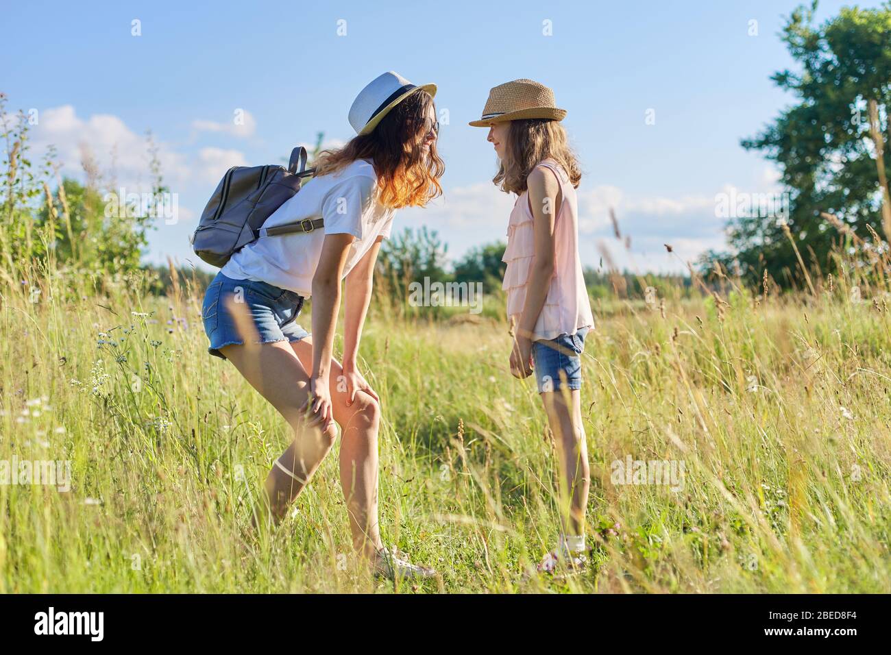 Niños felices dos niñas hermanas adolescentes y jóvenes riendo y divertirse en la pradera, el cielo azul, la naturaleza de verano. Estilo de vida activo y saludable, amigable f Foto de stock