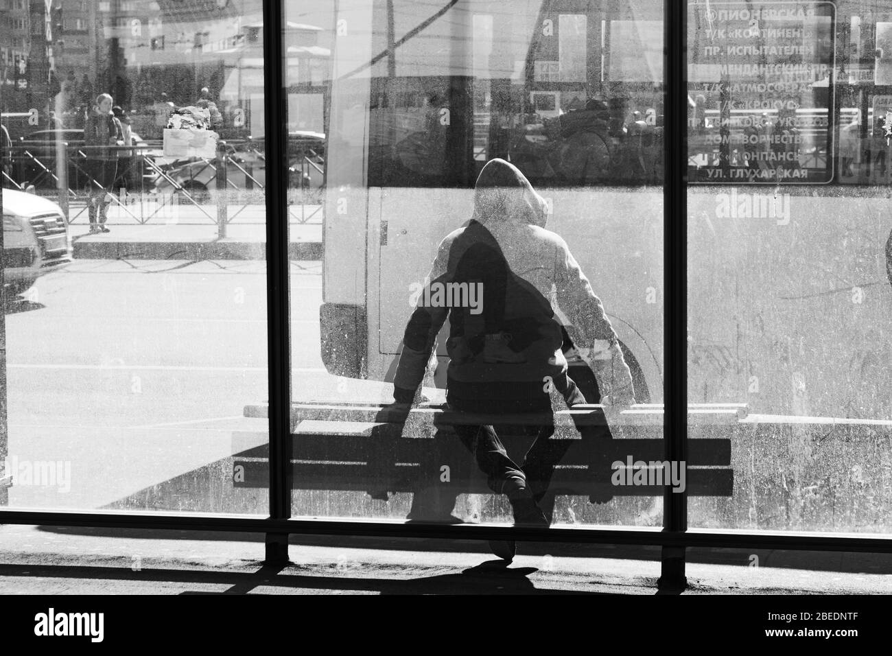 Un hombre está esperando un autobús en una parada de autobús detrás de un cristal salpicado de barro Foto de stock