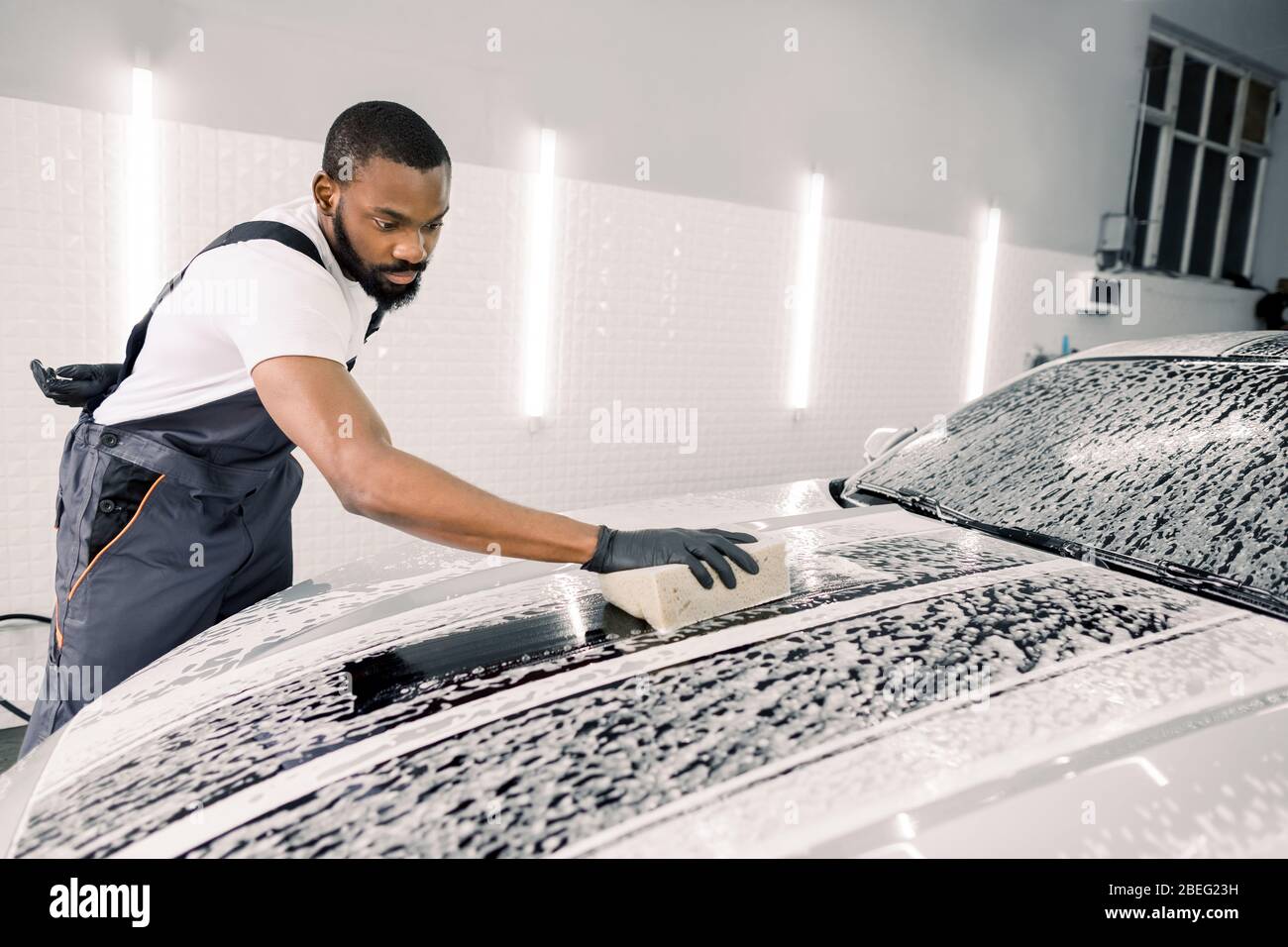 Lavar el coche y limpiar con jabón y esponja. Joven trabajador africano  americano concentrado, con overoles grises y guantes negros lavando la  capucha de coche jabonosa Fotografía de stock - Alamy