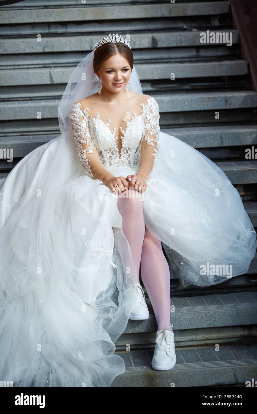 La novia con un vestido de boda blanco y zapatillas de deporte blancas se  sienta en los escalones de un edificio grande Fotografía de stock - Alamy