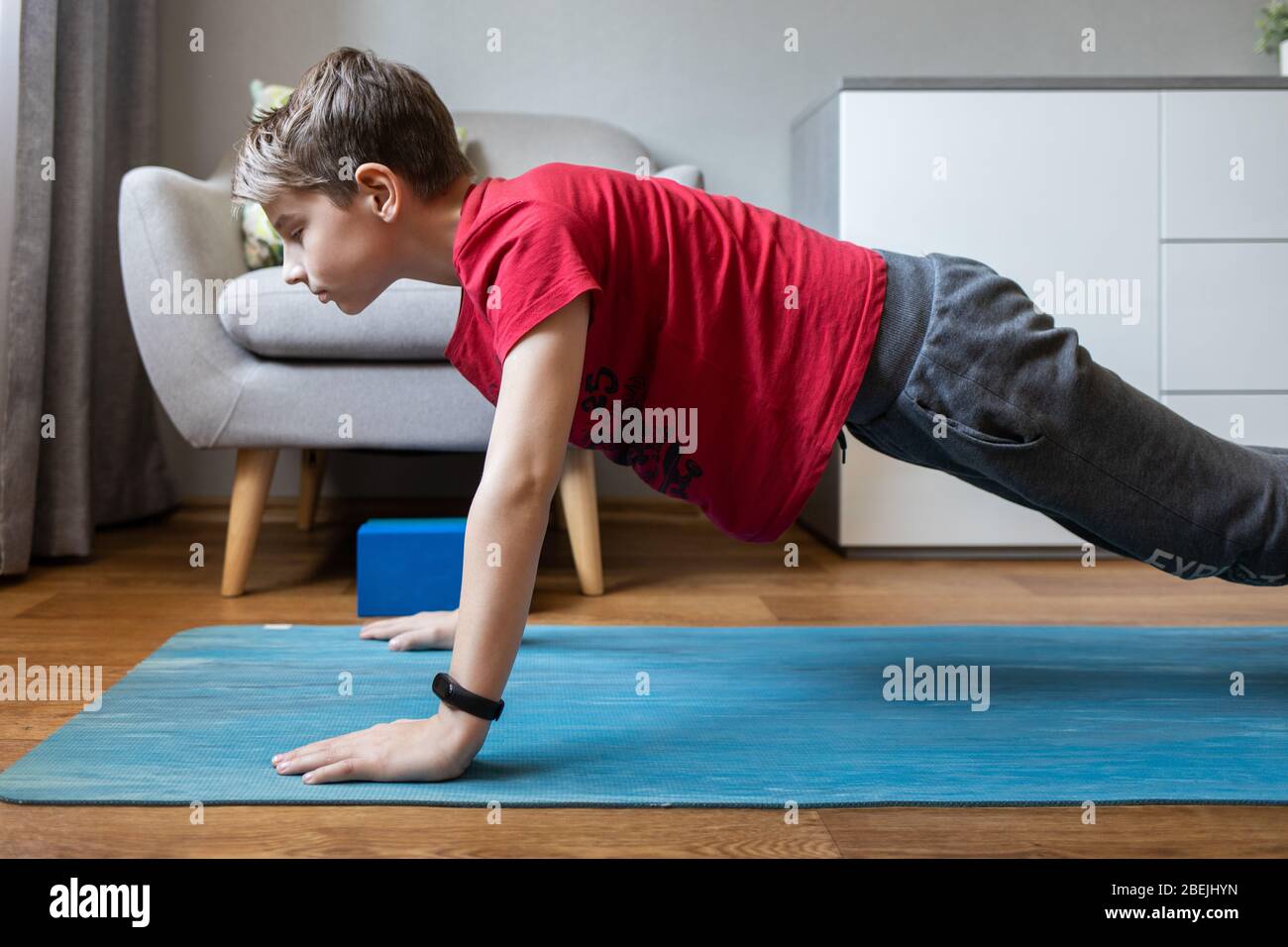 Un niño pequeño en una alfombrilla de yoga en casa sosteniendo una postura de tabla. Actividad física infantil en casa en cuarentena Foto de stock