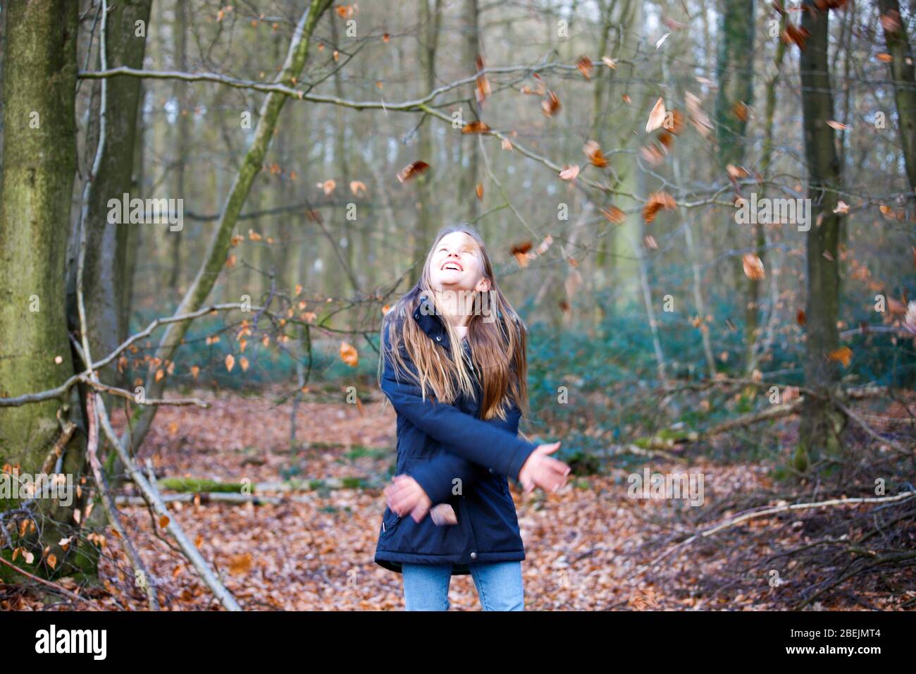 una niña se encuentra en el bosque y lanza hojas al aire Foto de stock
