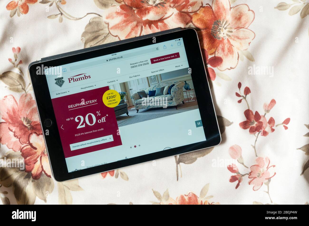 El sitio web de la empresa de tapicería de plumbs se muestra en un iPad tablet con cubierta de tela estampada en el fondo. Foto de stock