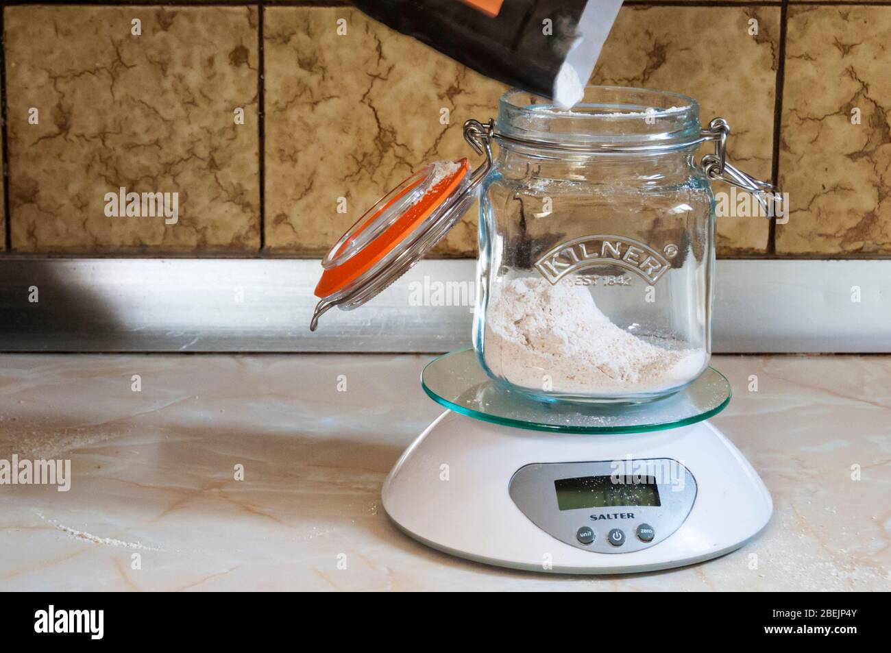 Preparación de un iniciador de masa fermentada - medición de la harina en un tarro de cristal de horno. Foto de stock