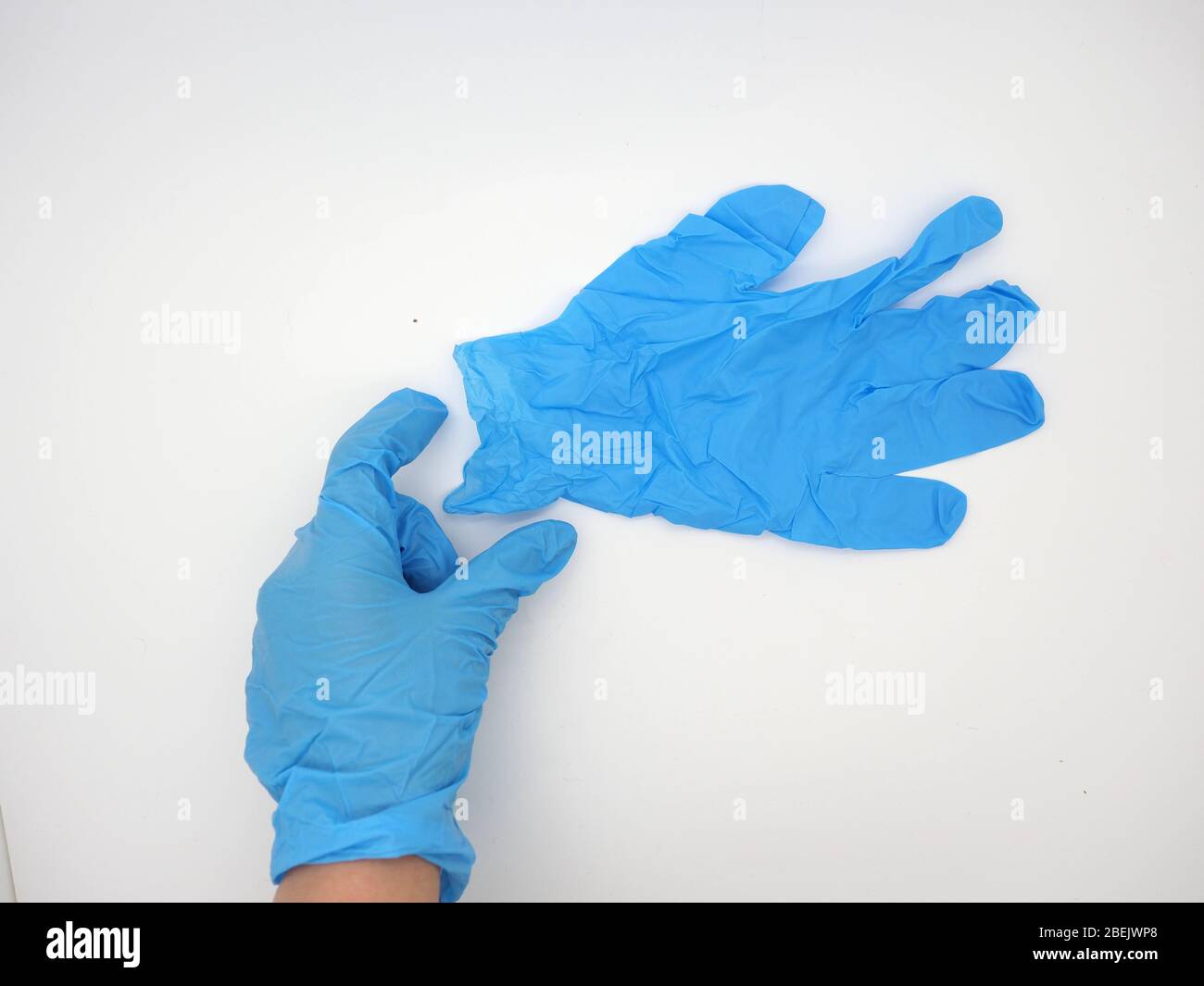 Mano con un guante desechable azul (PPE) alcanzando y recogiendo un par de gafas protectoras, Londres, Reino Unido Foto de stock