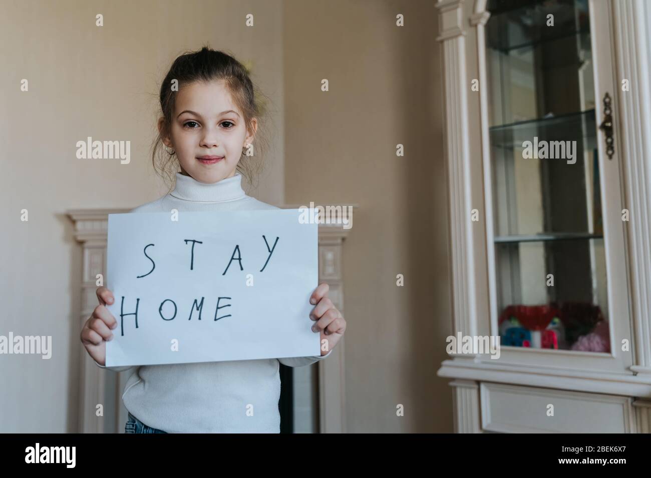 Concepto de estancia en casa. Pequeña niña sosteniendo signo diciendo permanecer en casa para la protección contra virus y cuidar de su salud de COVID-19. Foto de stock