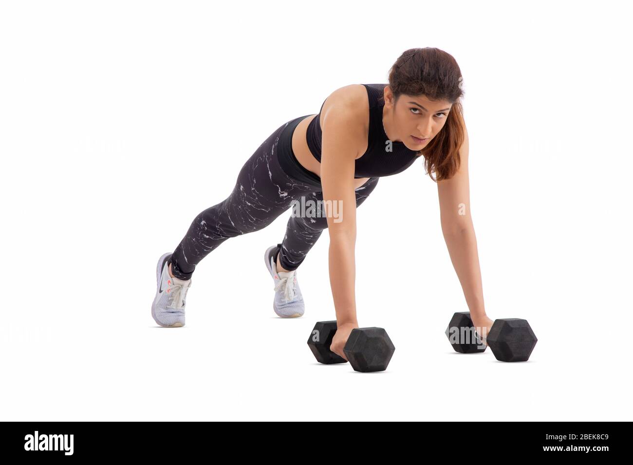 Mujer haciendo pushups con pesas sobre un fondo blanco. Foto de stock