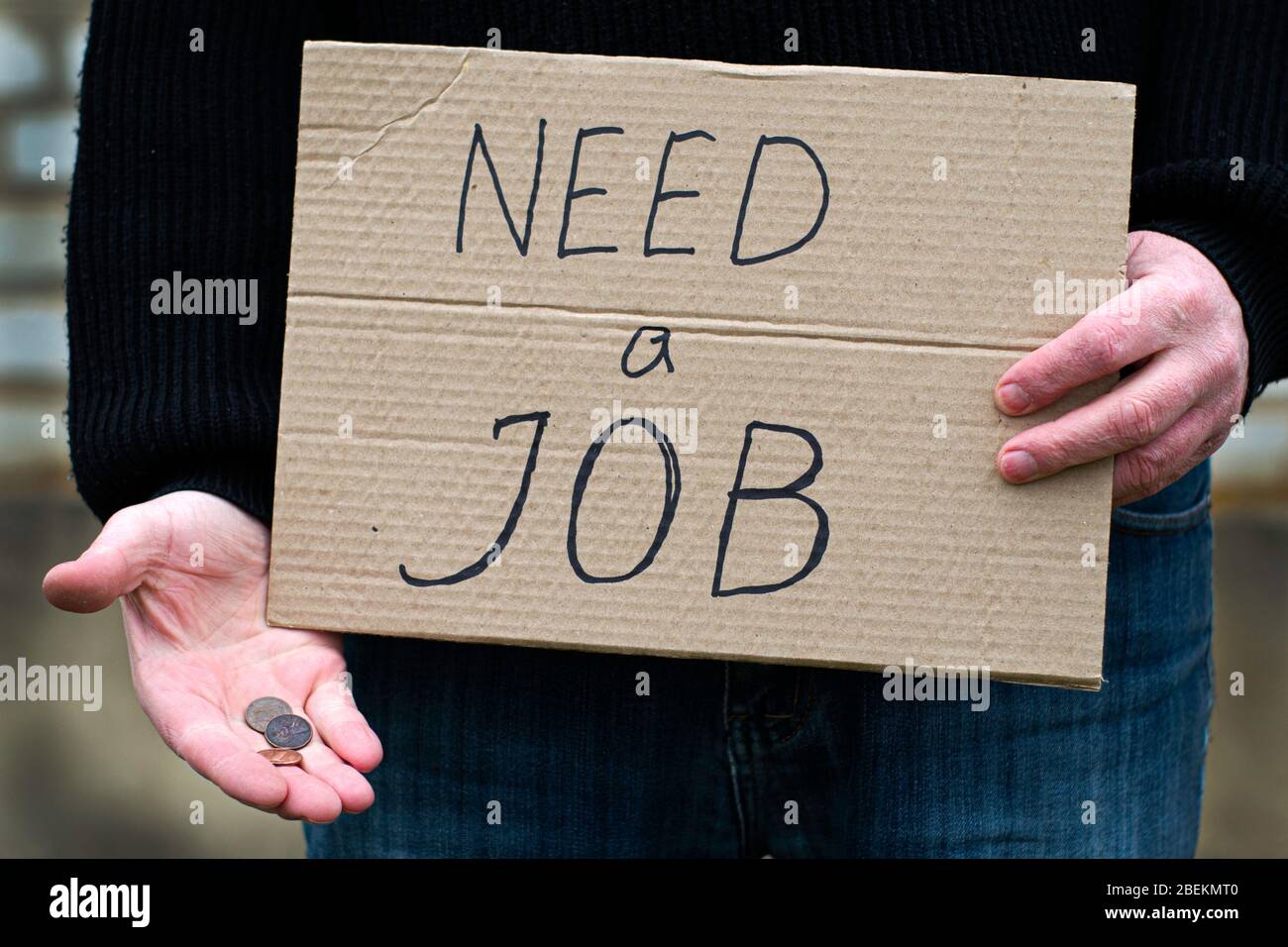 el desempleado sostiene en su mano la tableta de cartón con la inscripción necesita un trabajo en su otra mano las monedas restantes Foto de stock