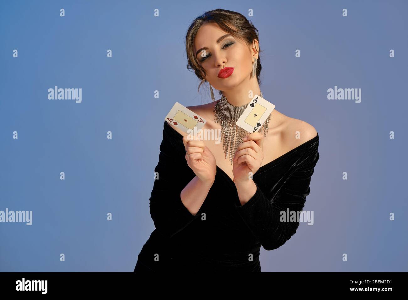 Dama morena con hombros desnudos, vestido negro y joyería. Ella te besa,  mostrando dos ases, posando sobre fondo azul. Póquer, casino. Primer plano  Fotografía de stock - Alamy