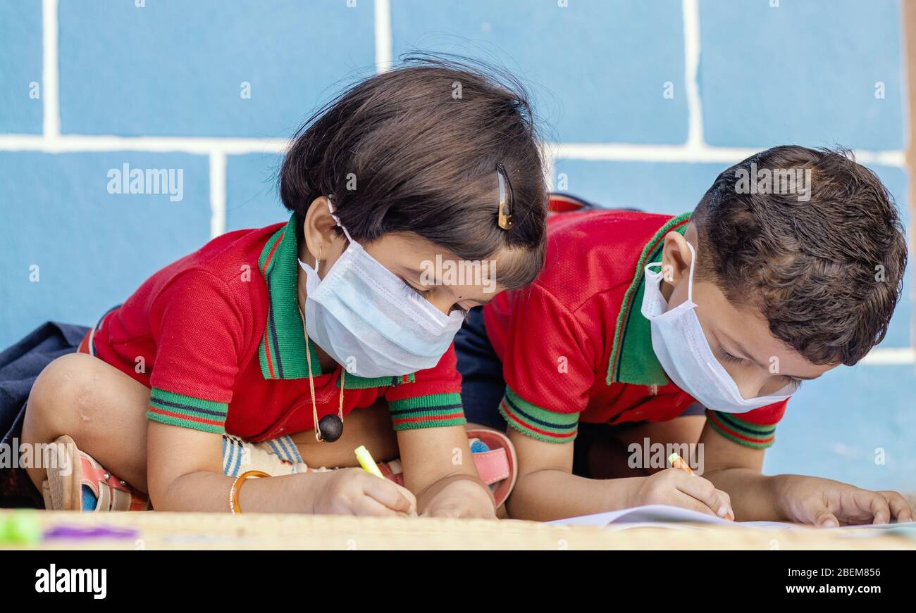 Niños ocupados en escribir con máscara médica debido a covid-19 o brote de coronavirus o pandemia en la escuela - niños que pintan en casa durante Foto de stock