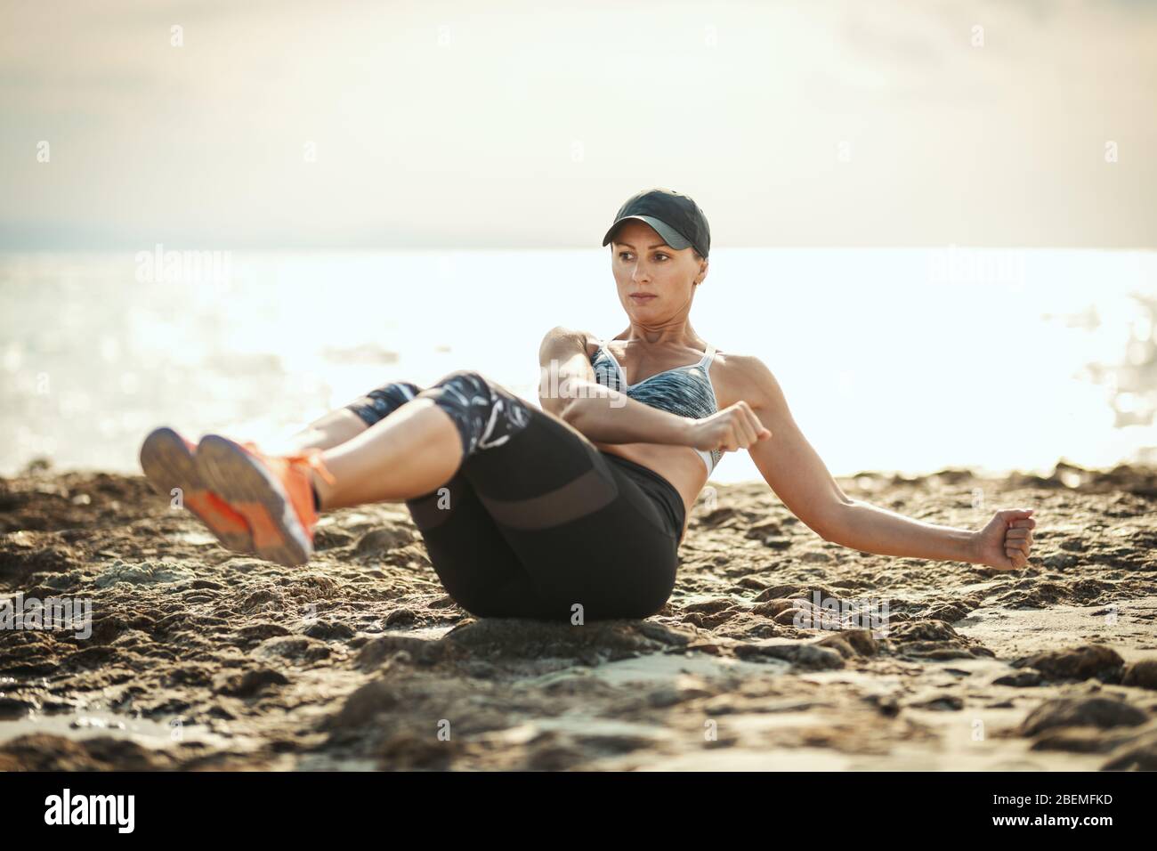 Una hermosa mujer joven está haciendo entrenamiento cruzado en la playa del mar en el día soleado del verano. Foto de stock