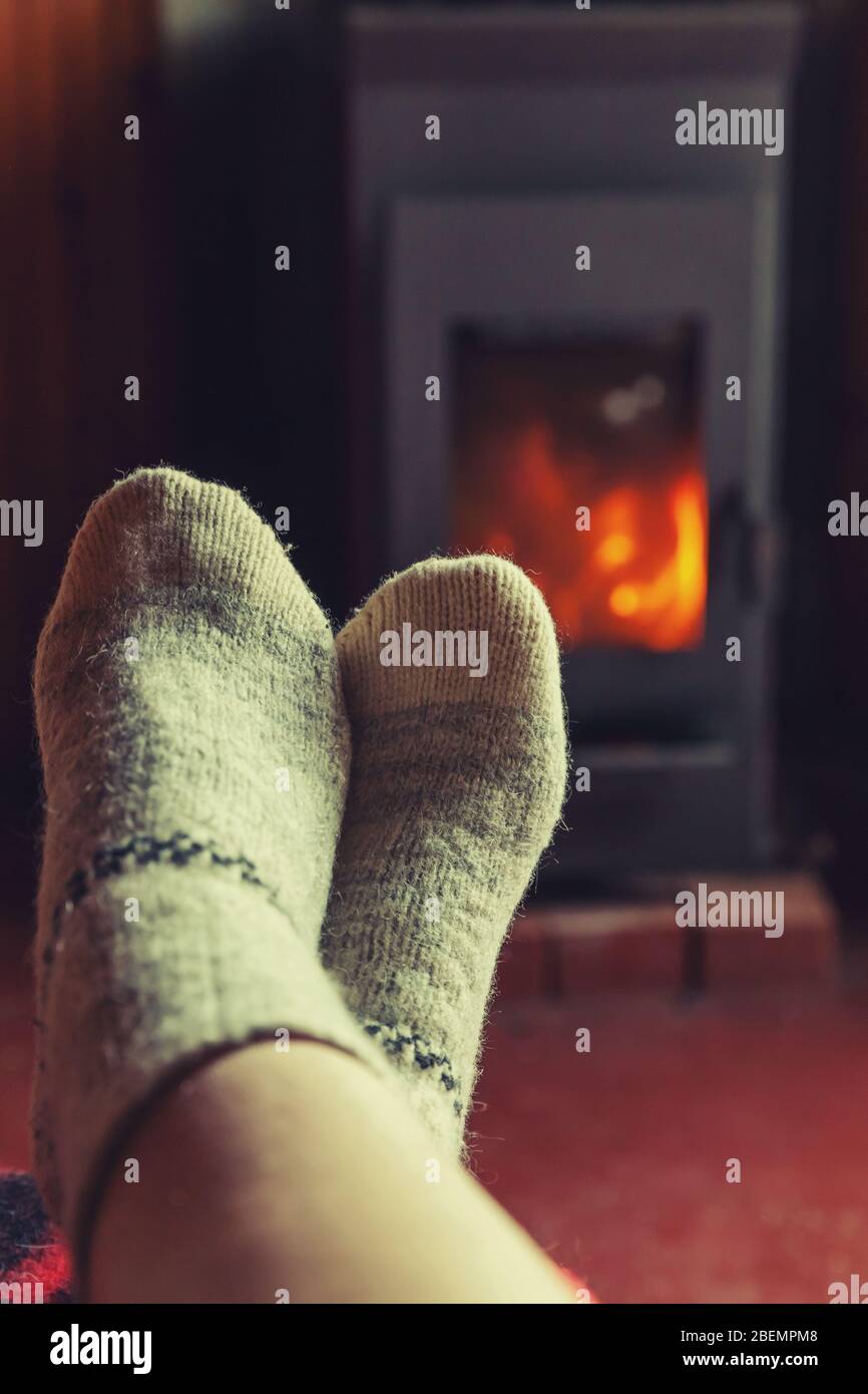 Pies piernas en ropa de invierno calcetines de lana en la chimenea de fondo. Mujer sentada en su casa en el invierno o el otoño tarde relajándose y calentando. El invierno y el frío concepto. La víspera de Navidad Hygge Foto de stock