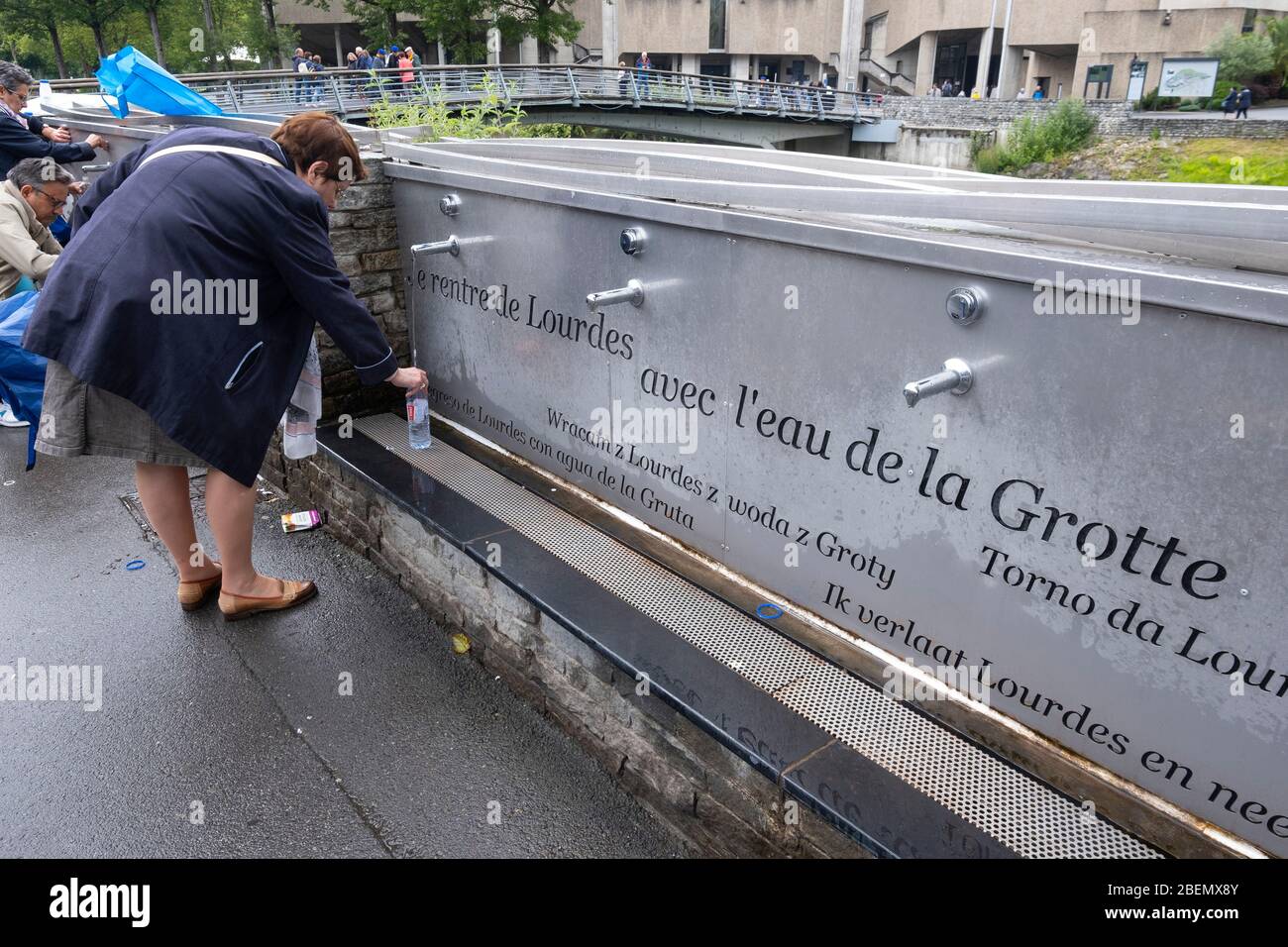 Peregrino llenando una botella de agua Santa de los grifos en el santuario de Lourdes, Francia, Europa Foto de stock