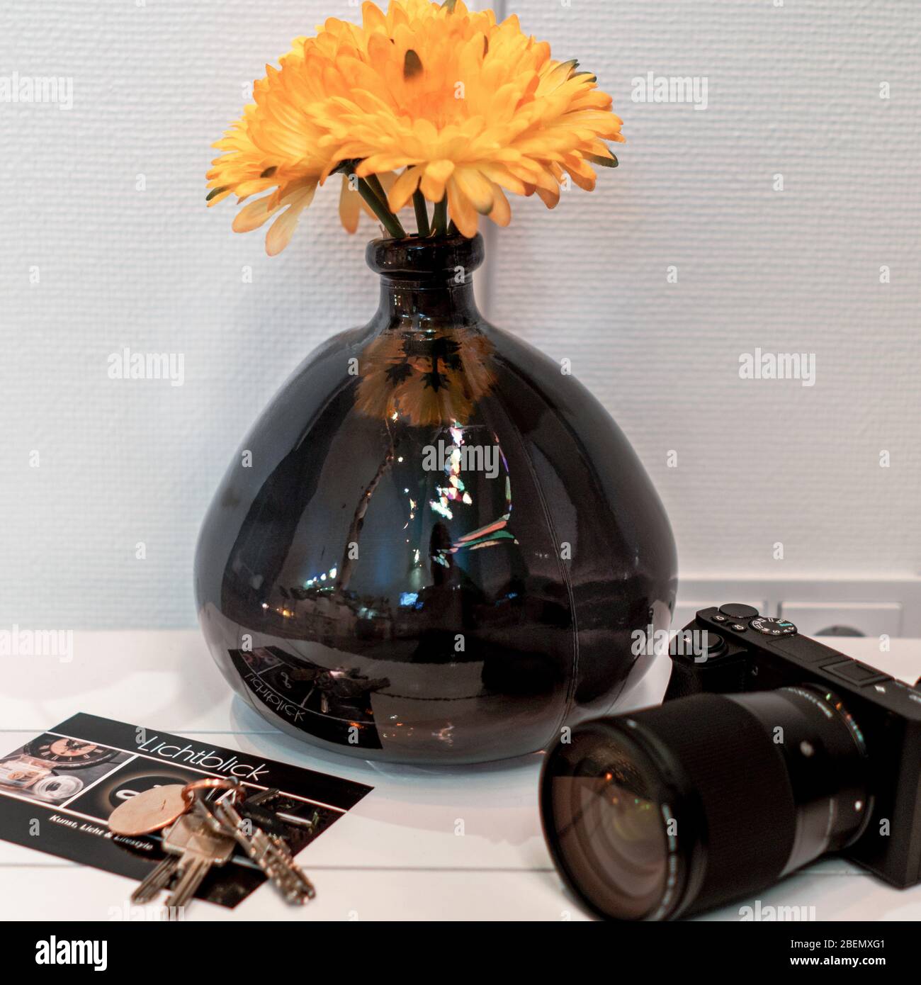 Jarrón de cristal negro sin forma con flor amarilla en la parte posterior  de un lateral con postal y cámara Fotografía de stock - Alamy