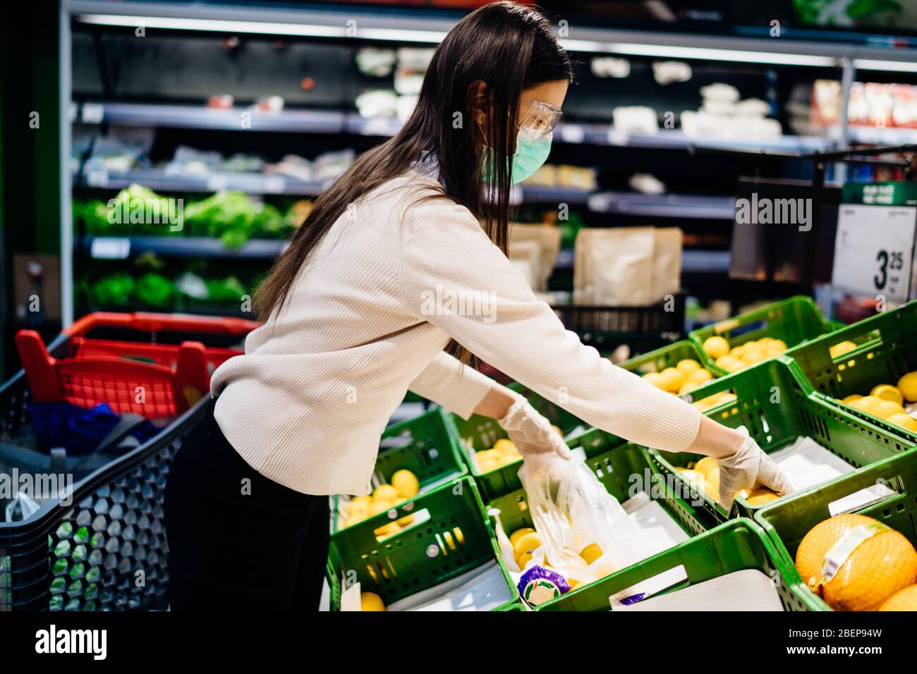 Mujer con máscara protectora compra en supermercado de comestibles para productos frescos, presupuesto de compras de cítricos durante la pandemia. Fuente natural de vitami Foto de stock