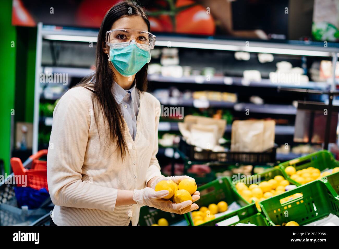 Mujer con máscara protectora compra en supermercado de comestibles para productos frescos, presupuesto de compras de cítricos durante la pandemia. Fuente natural de vitami Foto de stock