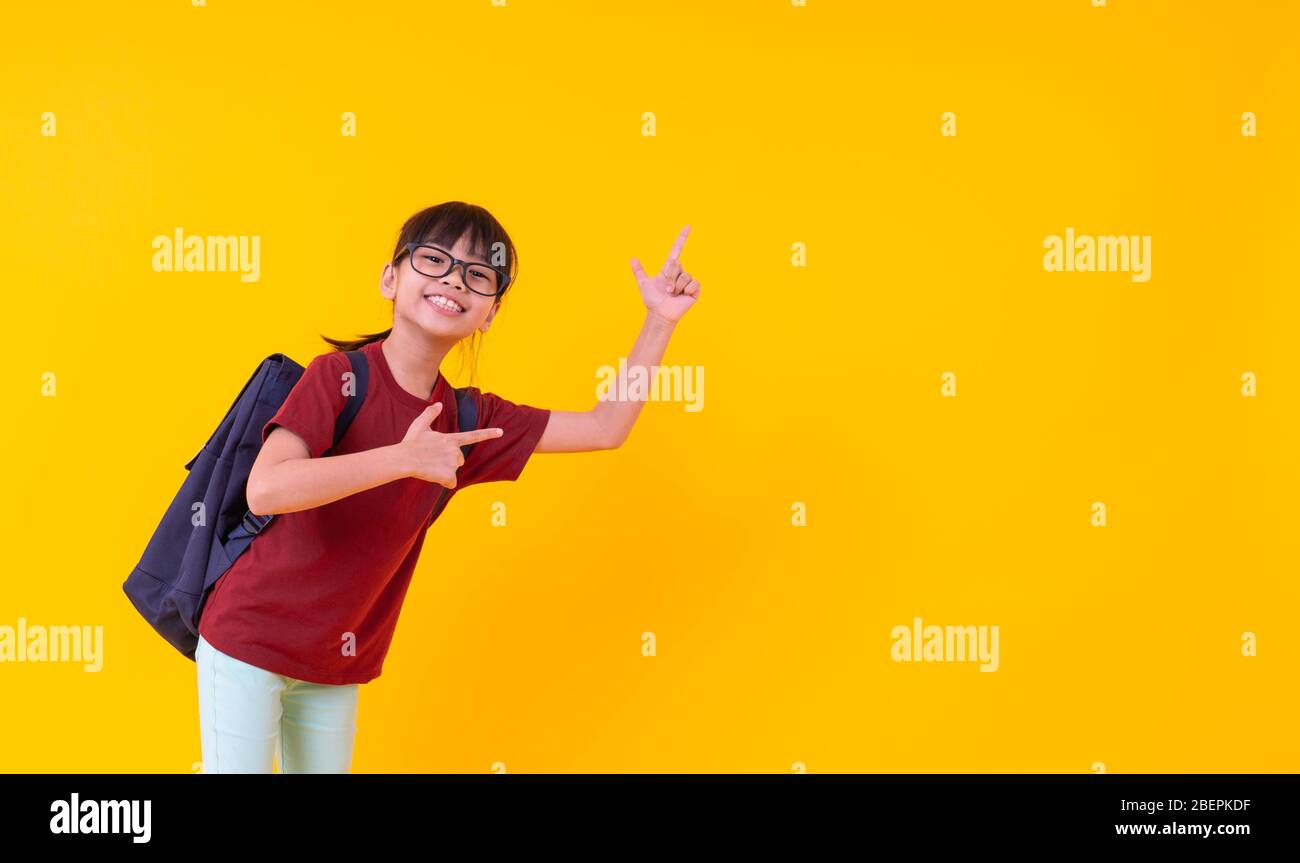 Retrato de una joven estudiante asiática señalando el espacio de copia, un  niño tailandés bonito en camisa roja con bolsa de escuela mirando la cámara  y sonriendo en el reverso amarillo Fotografía