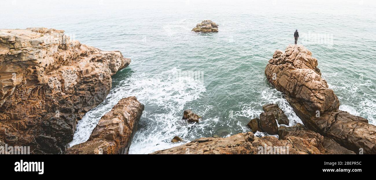 Hombre de pie sobre una roca a la orilla del mar. Fotografía de aventura. Imagen panorámica. Vistas panorámicas Foto de stock