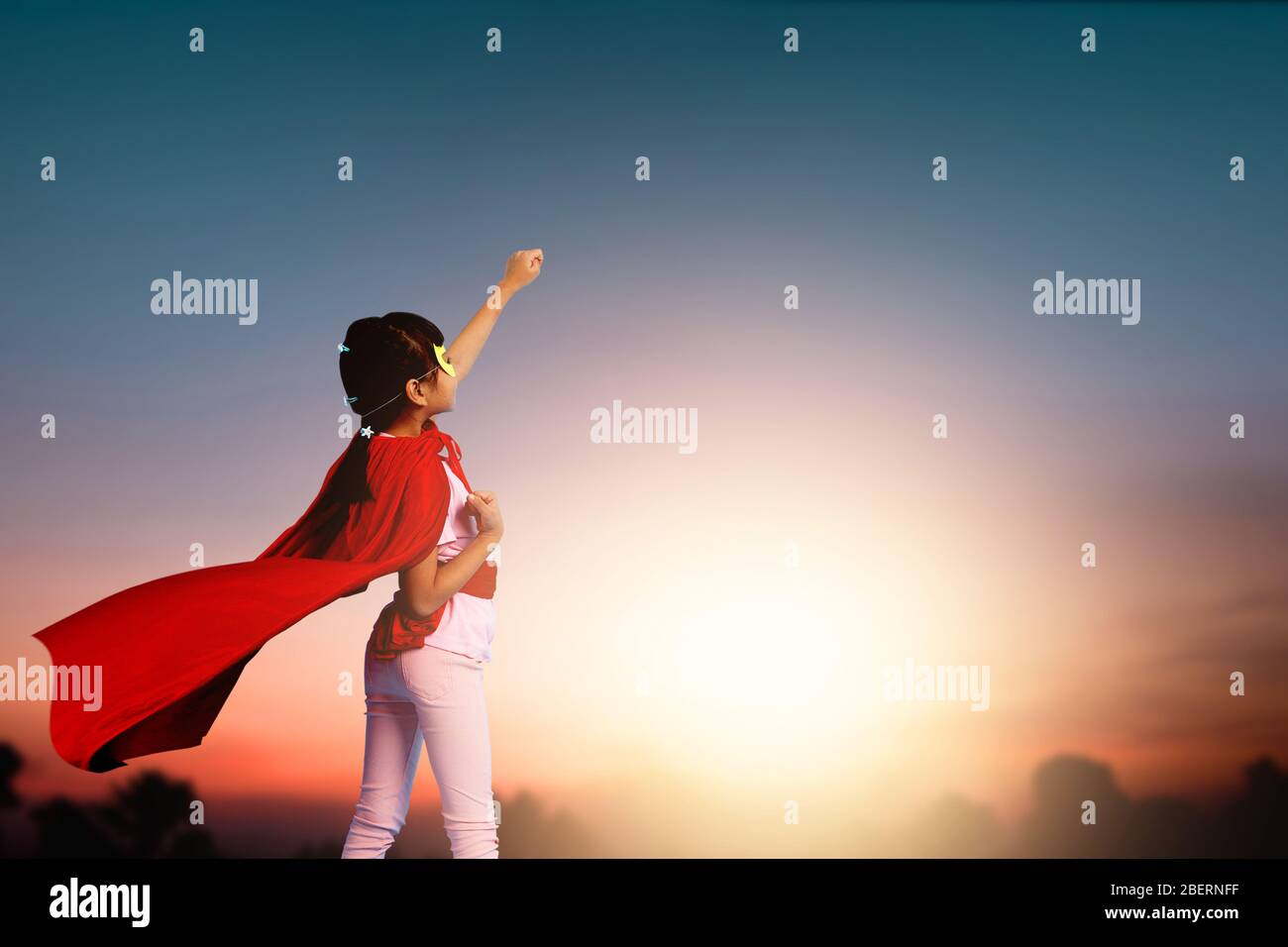 Super niña niño mostrar poder, niño pequeño con vestido rojo héroe mostrar mano hasta el cielo en el sol establecer, sueño activo y motivación idea concepto Foto de stock