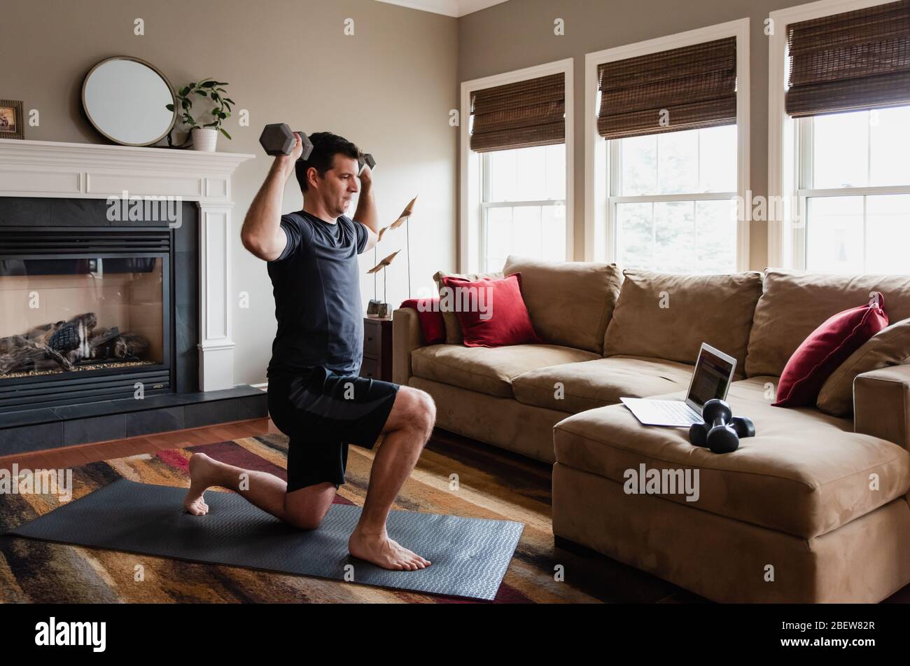 Hombre trabajando con pesas en casa usando el programa de ejercicios en línea. Foto de stock
