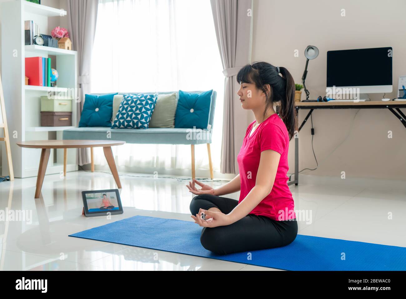 Mujer asiática haciendo ejercicio de yoga para alejarse de sus ordenadores para tomar descansos de ejercicios a mitad del día a través de las clases de videos de livestream en tabletas digitales d Foto de stock