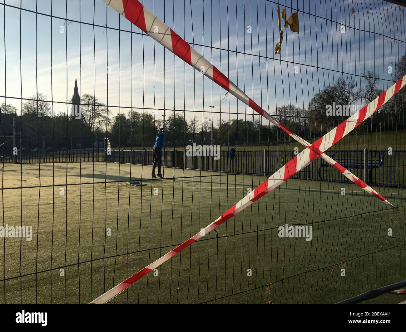 Glasgow, Reino Unido, 16 de abril de 2020. Un hombre hace ejercicios temprano por la mañana en Queen's Park, junto a cercas y cintas que muestran las restricciones en el campo de baloncesto/fútbol, para asegurar el distanciamiento social correcto del público y para prevenir reuniones de personas, durante la actual crisis de salud pandémica del Coronavirus COVID-19. Crédito de la foto: Sir-Hibbert/Alamy Live News. Foto de stock
