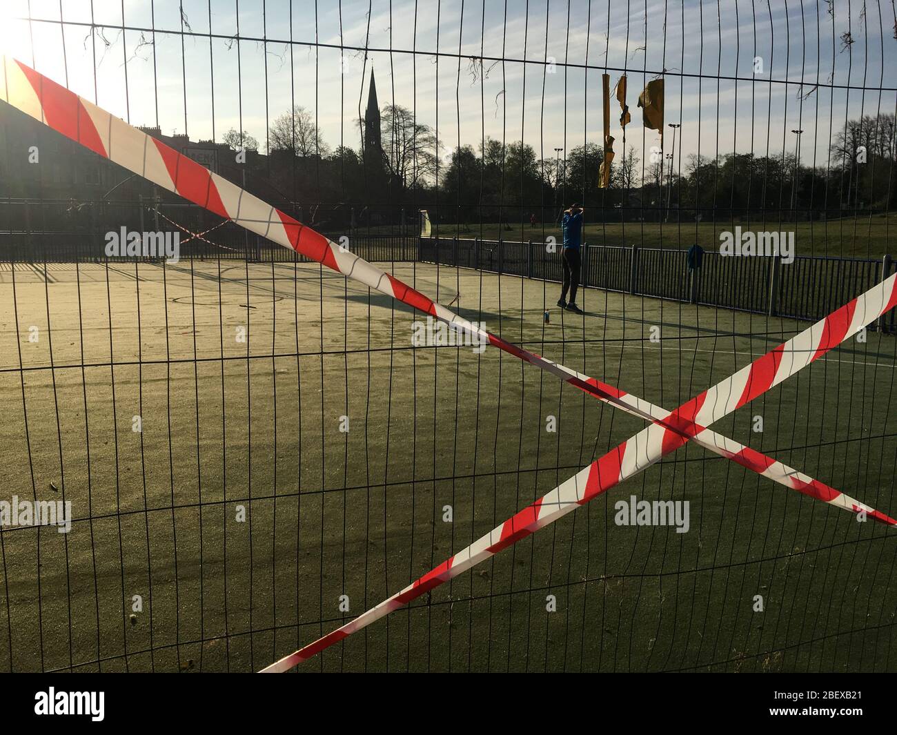 Glasgow, Reino Unido, 16 de abril de 2020. Un hombre hace ejercicios temprano por la mañana en Queen's Park, junto a cercas y cintas que muestran las restricciones en el campo de baloncesto/fútbol, para asegurar el distanciamiento social correcto del público y para prevenir reuniones de personas, durante la actual crisis de salud pandémica del Coronavirus COVID-19. Crédito de la foto: Sir-Hibbert/Alamy Live News. Foto de stock