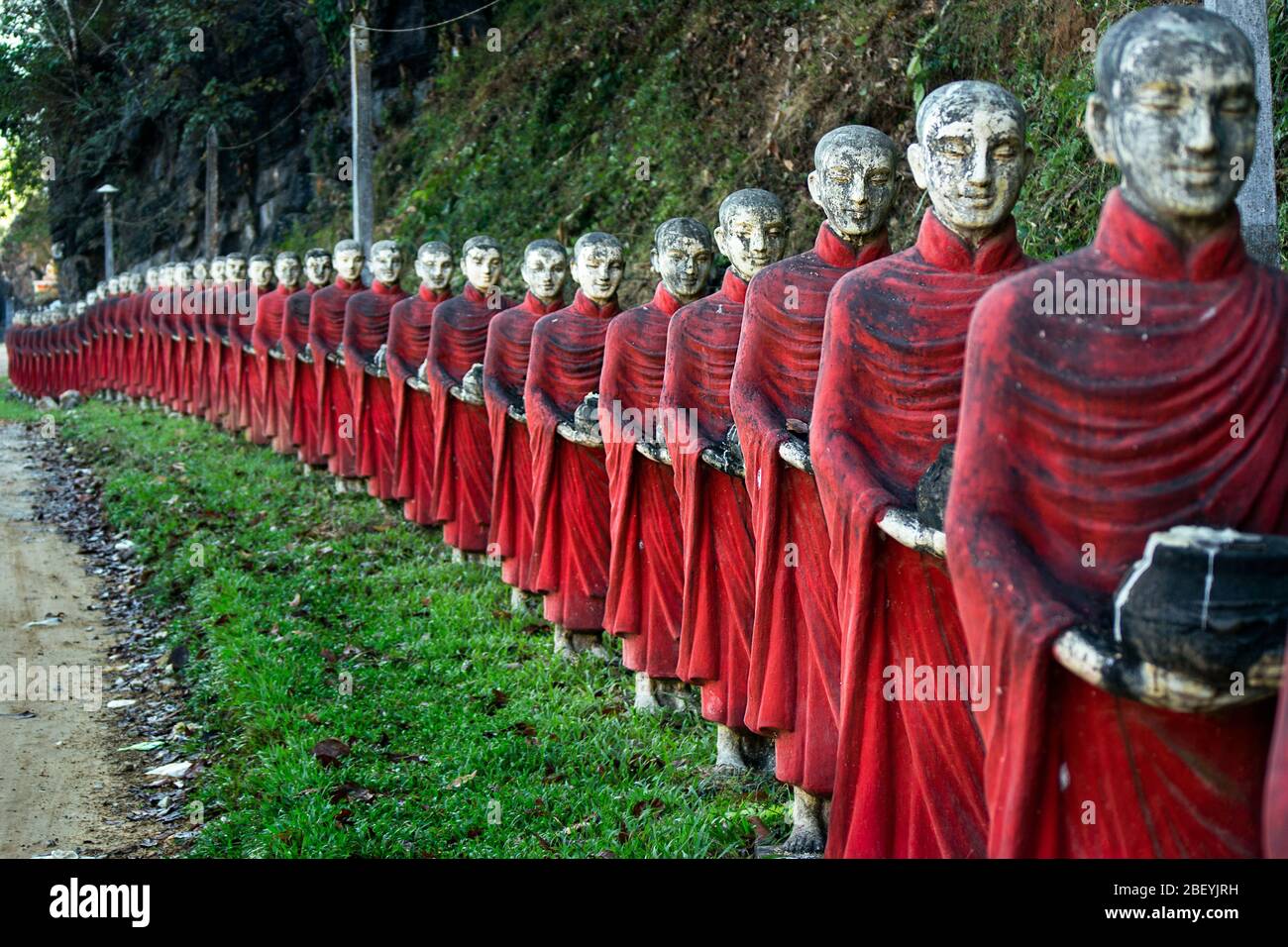Una larga fila de coloridas estatuas de monjes budistas en la entrada del templo de la cueva Kaw Ka Thaung. Foto de stock