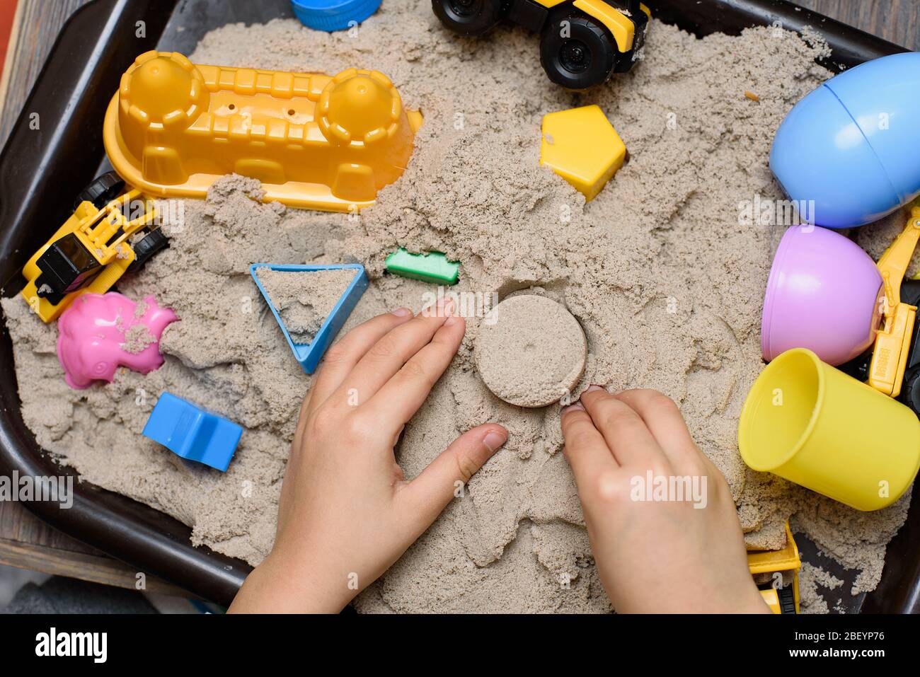 Niño jugando con arena cinética y maquinaria de construcción de juguetes.  Mano del niño en la arena de cerca. Vista superior, plano. Juego de mesa en  interior. Juego de creatividad Fotografía de