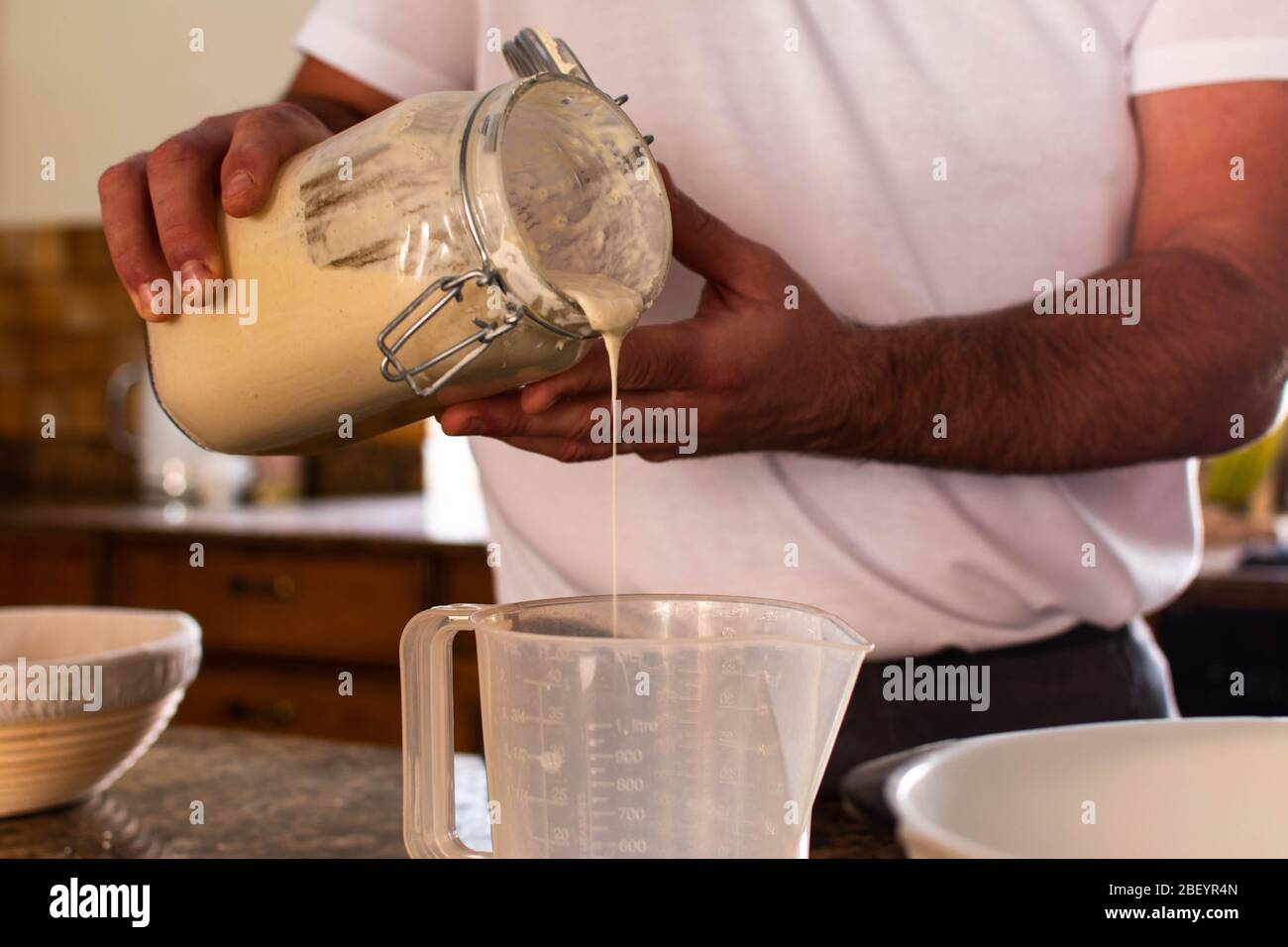 Cocina casera verter ingredientes en una jarra medidora mientras que él hace pan para rascar Foto de stock