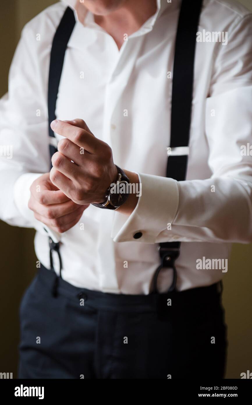 Mañana novio. Un hombre con una camisa blanca y tirantes pone un reloj en su muñeca. De cerca, sin cara. Preparación para la boda Fotografía de Alamy