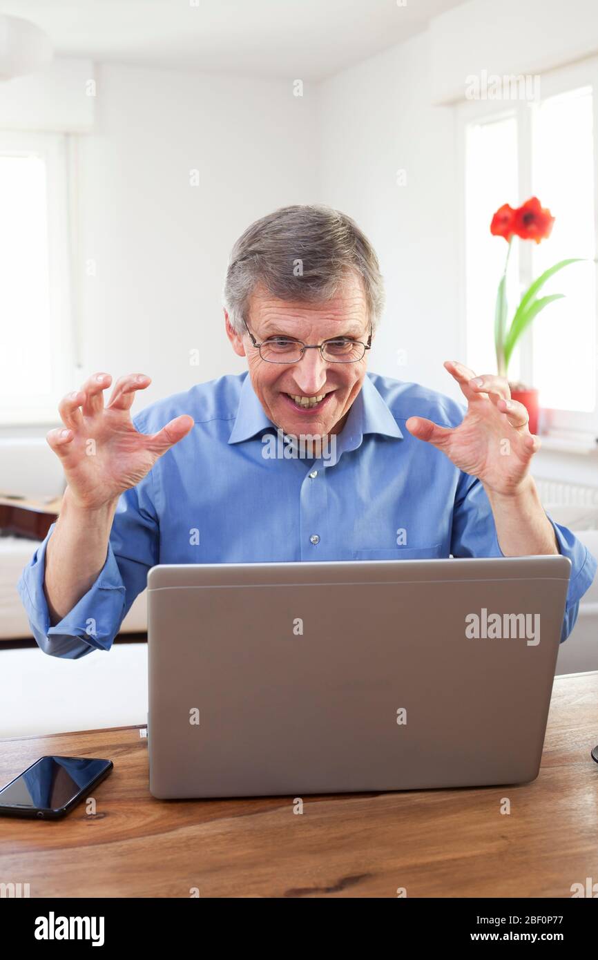 Un hombre de negocios molesto sentado en una mesa con un ordenador portátil en una luminosa sala de estar en casa - centrarse en la cara Foto de stock