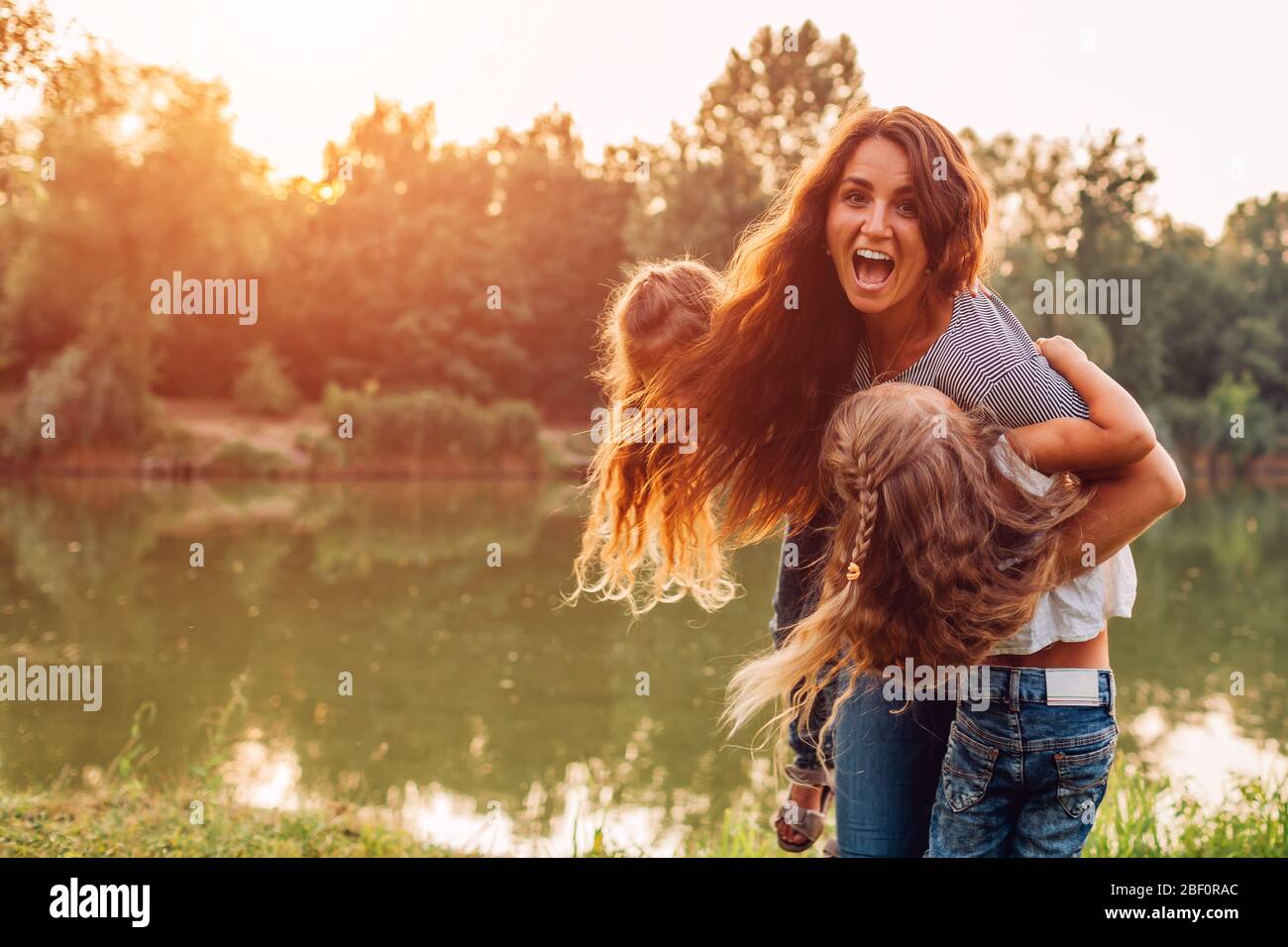 Día de la madre. Familia jugando y divertirse en el lago de primavera. Madre sosteniendo y girando alrededor de las hijas al aire libre. Foto de stock