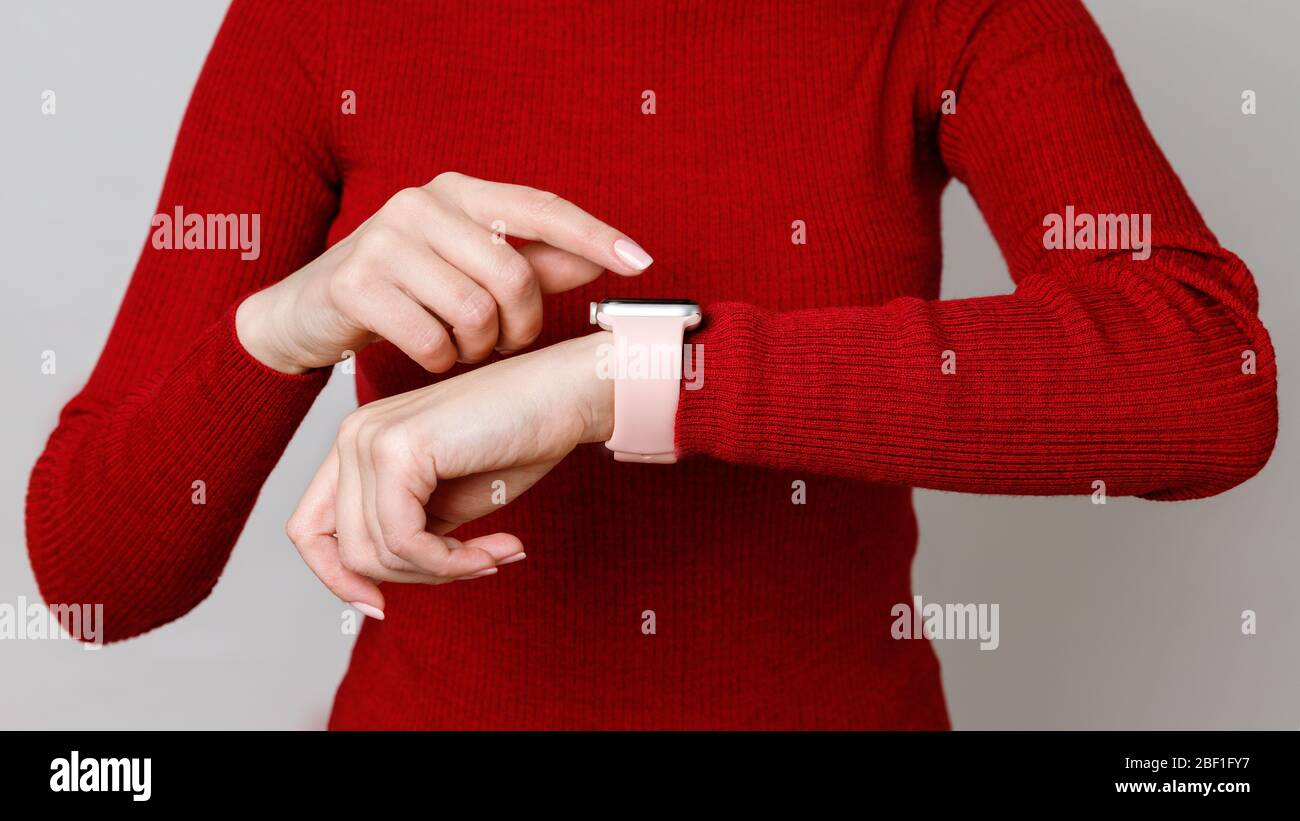 Foto recortada de mujer tocando, estableciendo o usando su smartwatch en su muñeca, comprobando el tiempo, sobre fondo rojo de cuello de cisne Foto de stock