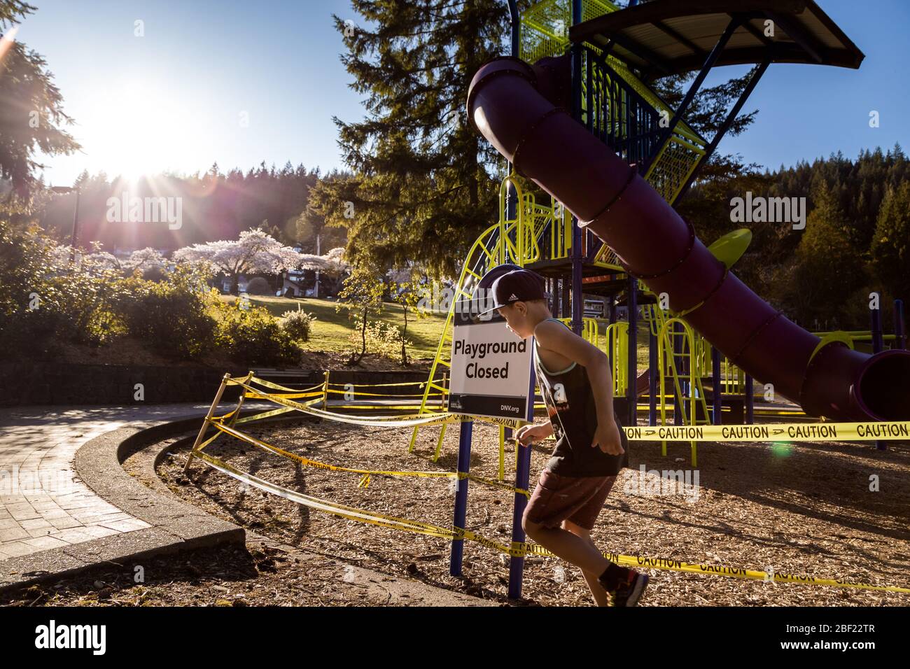 NORTH VANCOUVER, BC, CANADÁ - 11 DE ABRIL de 2020: Los niños juegan fuera de un parque infantil cerrado en un parque público North Vancouver alineado con cinta de precaución Foto de stock