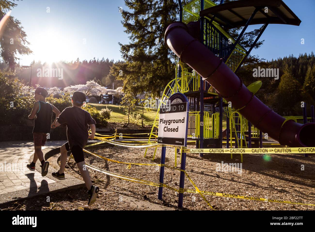 NORTH VANCOUVER, BC, CANADÁ - 11 DE ABRIL de 2020: Los niños juegan fuera de un parque infantil cerrado en un parque público North Vancouver alineado con cinta de precaución Foto de stock