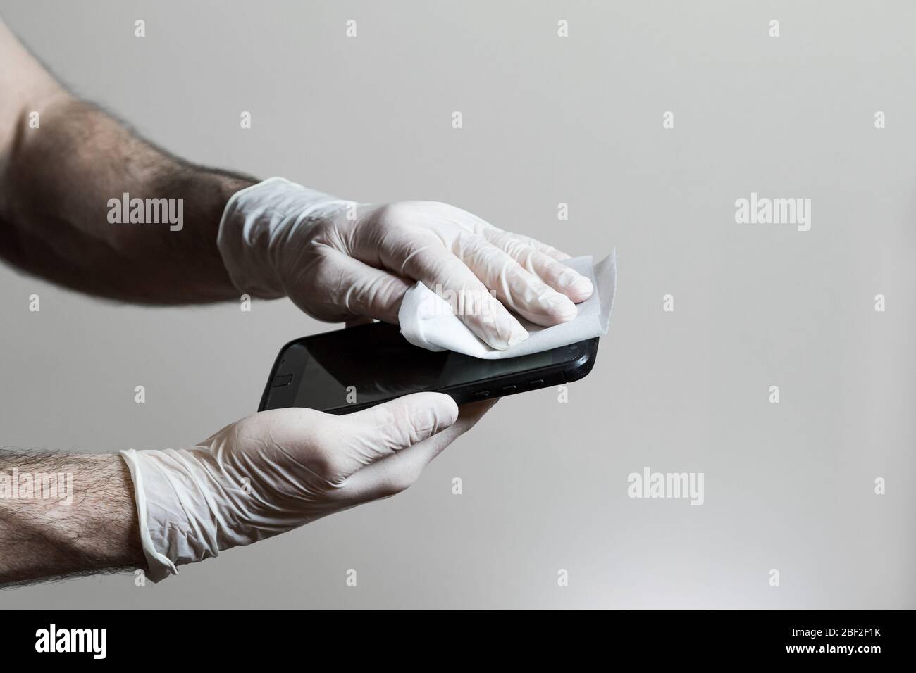 Un hombre manos con guantes de látex limpiando su teléfono celular con una toallita desinfectante durante la pandemia de Covid 19. Foto de stock