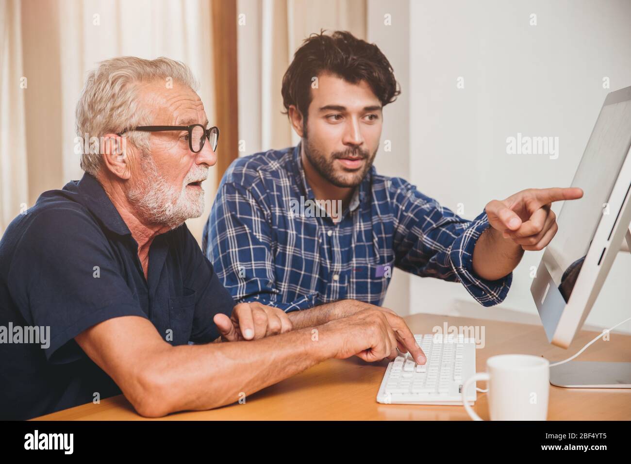 joven o hijo enseñando a su abuelo mayor papá a usar la computadora en casa. Foto de stock