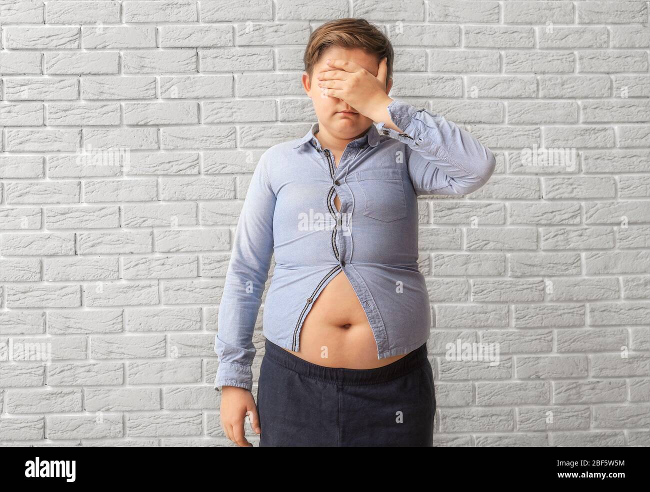 Niño triste con sobrepeso en ropa apretada cerca de la pared de ladrillo  Fotografía de stock - Alamy