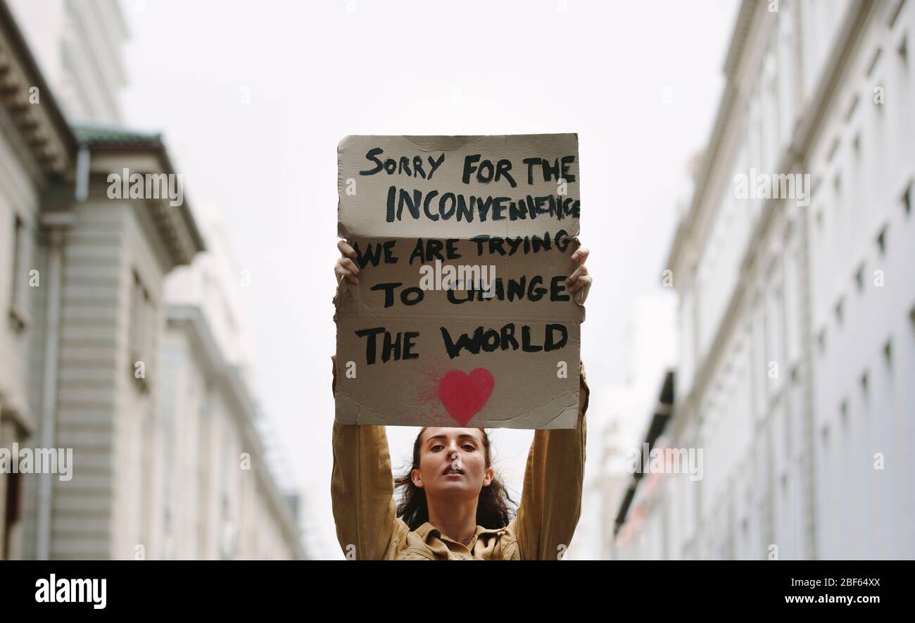 Mujer joven sosteniendo cartel y protestando. Manifestante que hace una protesta por el cambio climático. Foto de stock