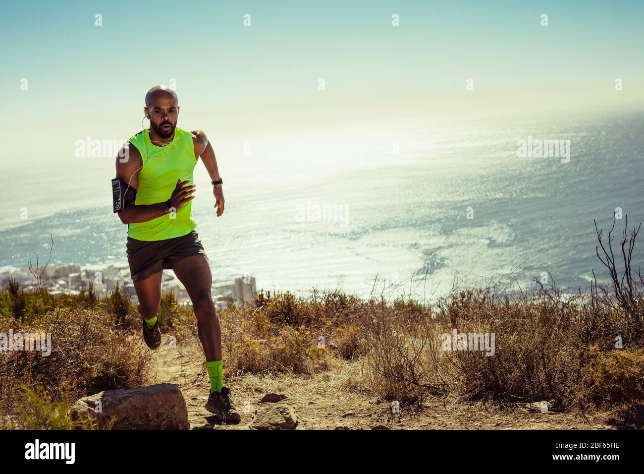 Hombre de fitness de longitud completa corriendo sobre un sendero rocoso en la montaña. Ajuste el joven corriendo por una colina. Foto de stock